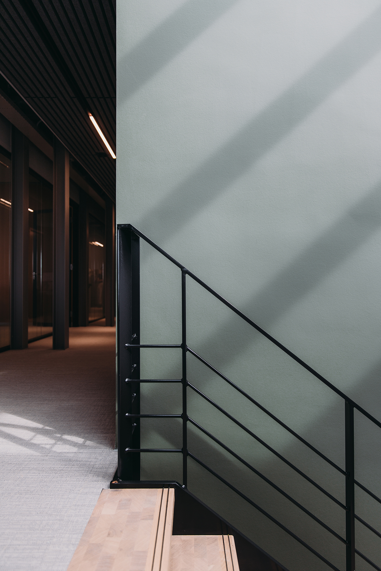 Steel railing with horizontal bars along a wall with diagonal shadow patterns from overhead skylights