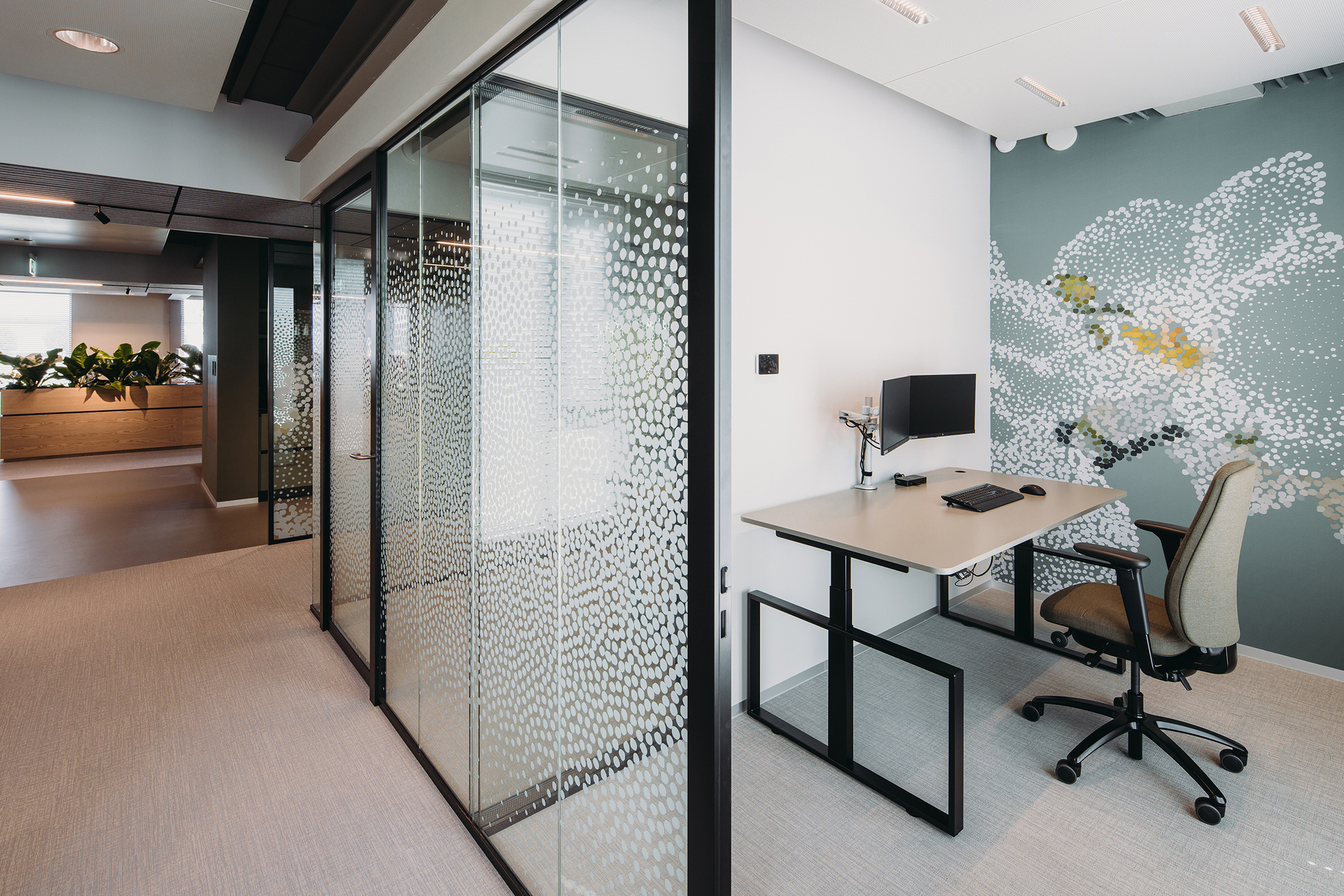Office workstation beside black-framed glass partitions with dotted film pattern and wall mural beyond