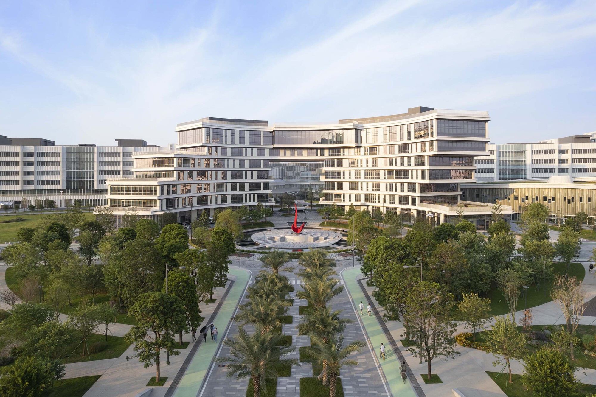 Symmetrical campus buildings flanking a central plaza with fountain and palm-lined pedestrian paths