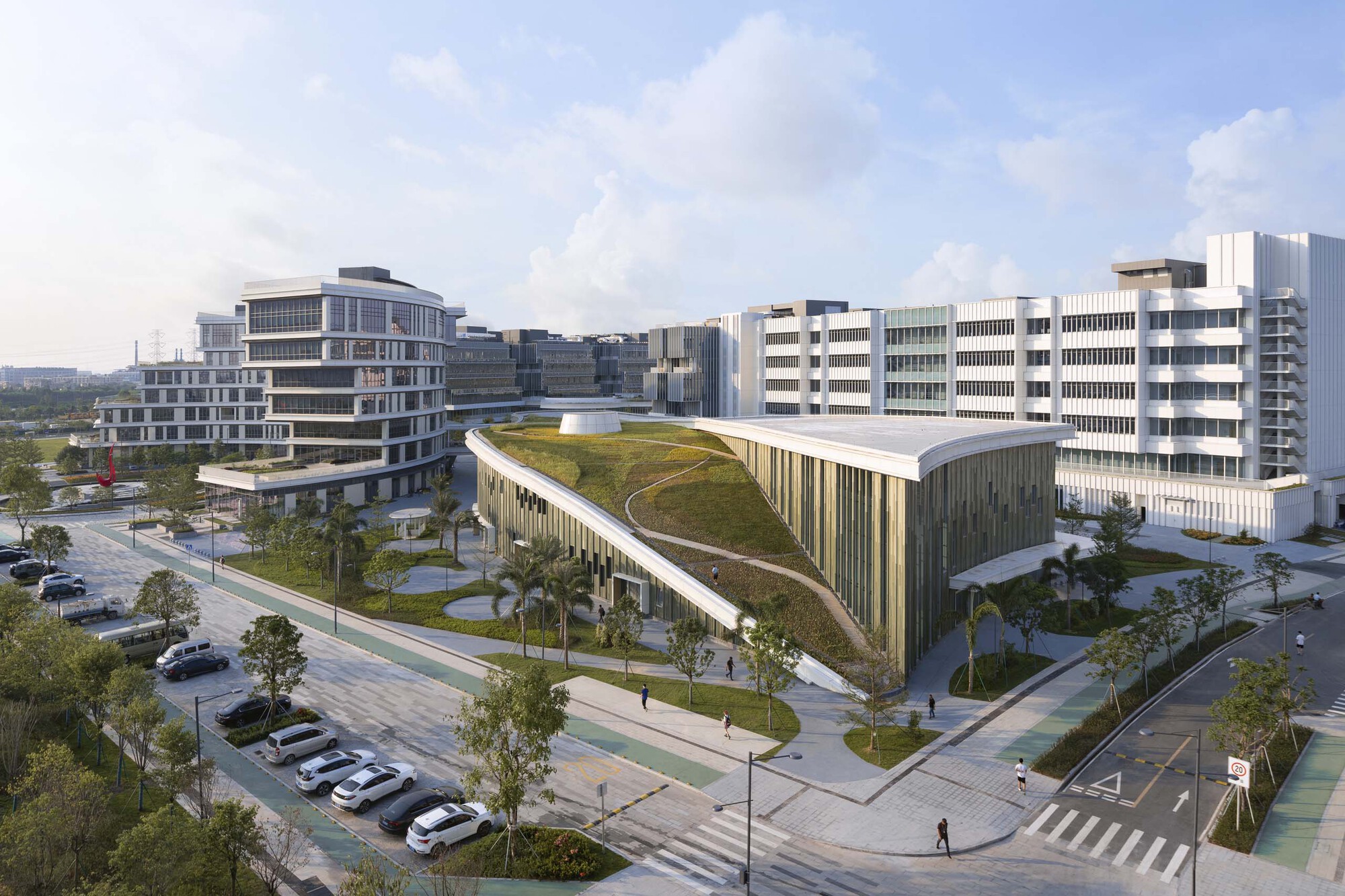Street corner view of a green roof pavilion with vertical louvers and parked cars