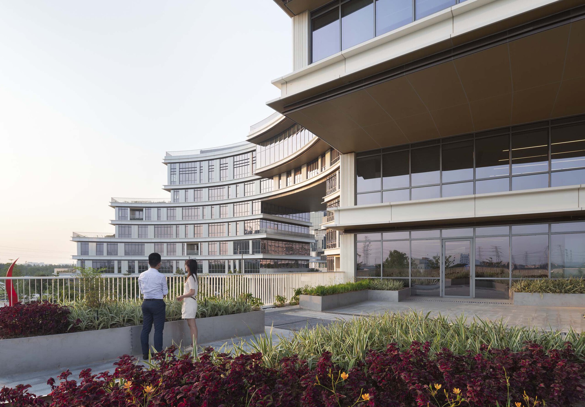 Rooftop terrace with planted beds and two people looking toward horizontal facade bands at dusk