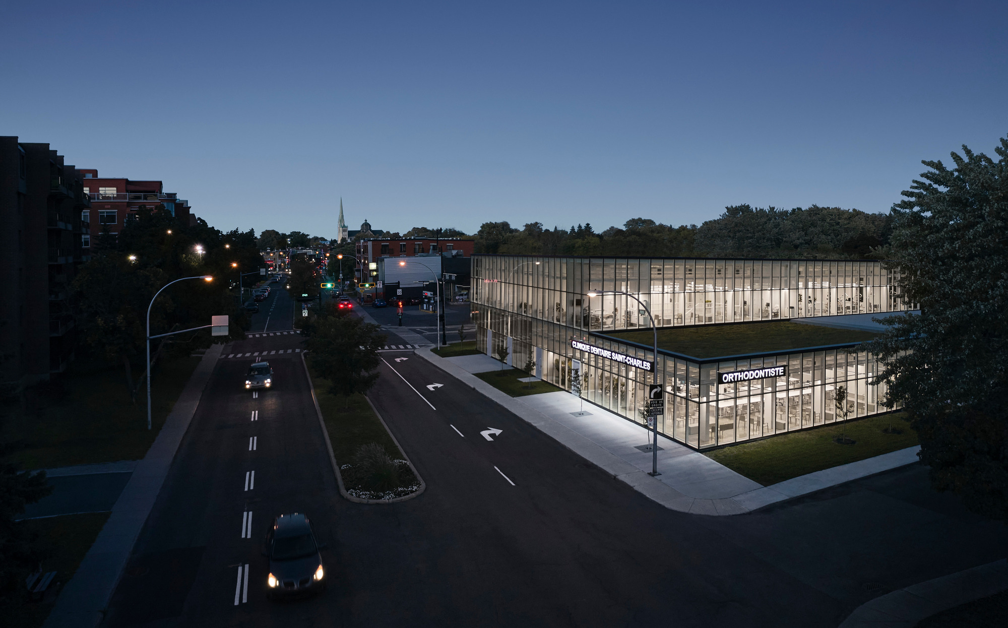 Corner view of the illuminated glass facade facing the street at twilight with traffic passing