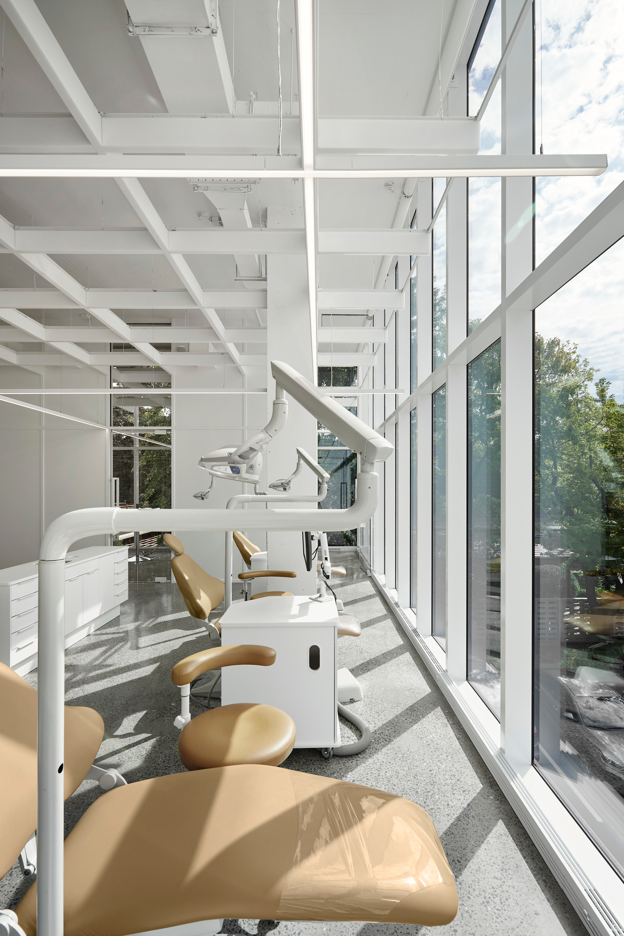 Corner workspace with dental chairs upholstered in tan vinyl beside a floor-to-ceiling glass curtain wall