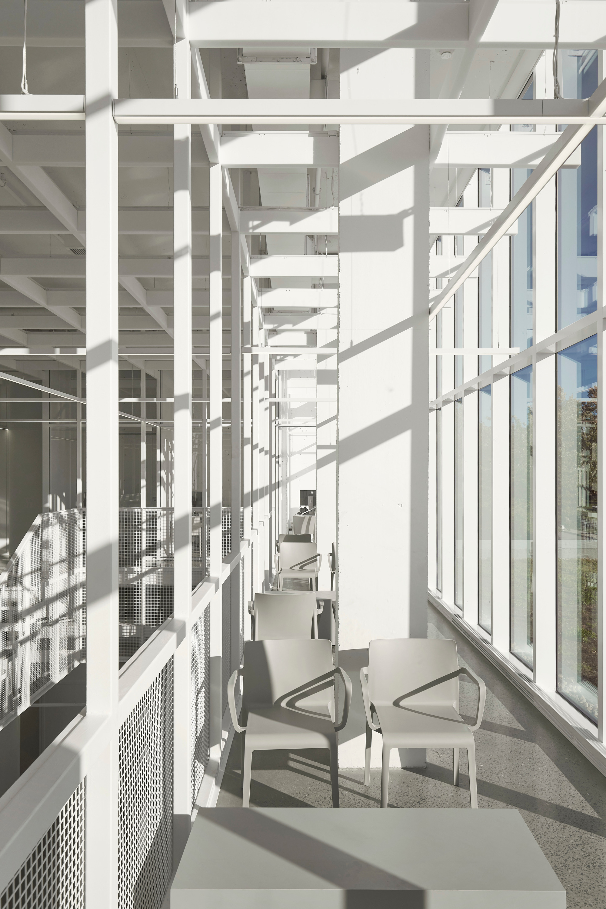 Narrow corridor along the glazed facade with perforated metal balustrade casting sharp shadows on the terrazzo floor