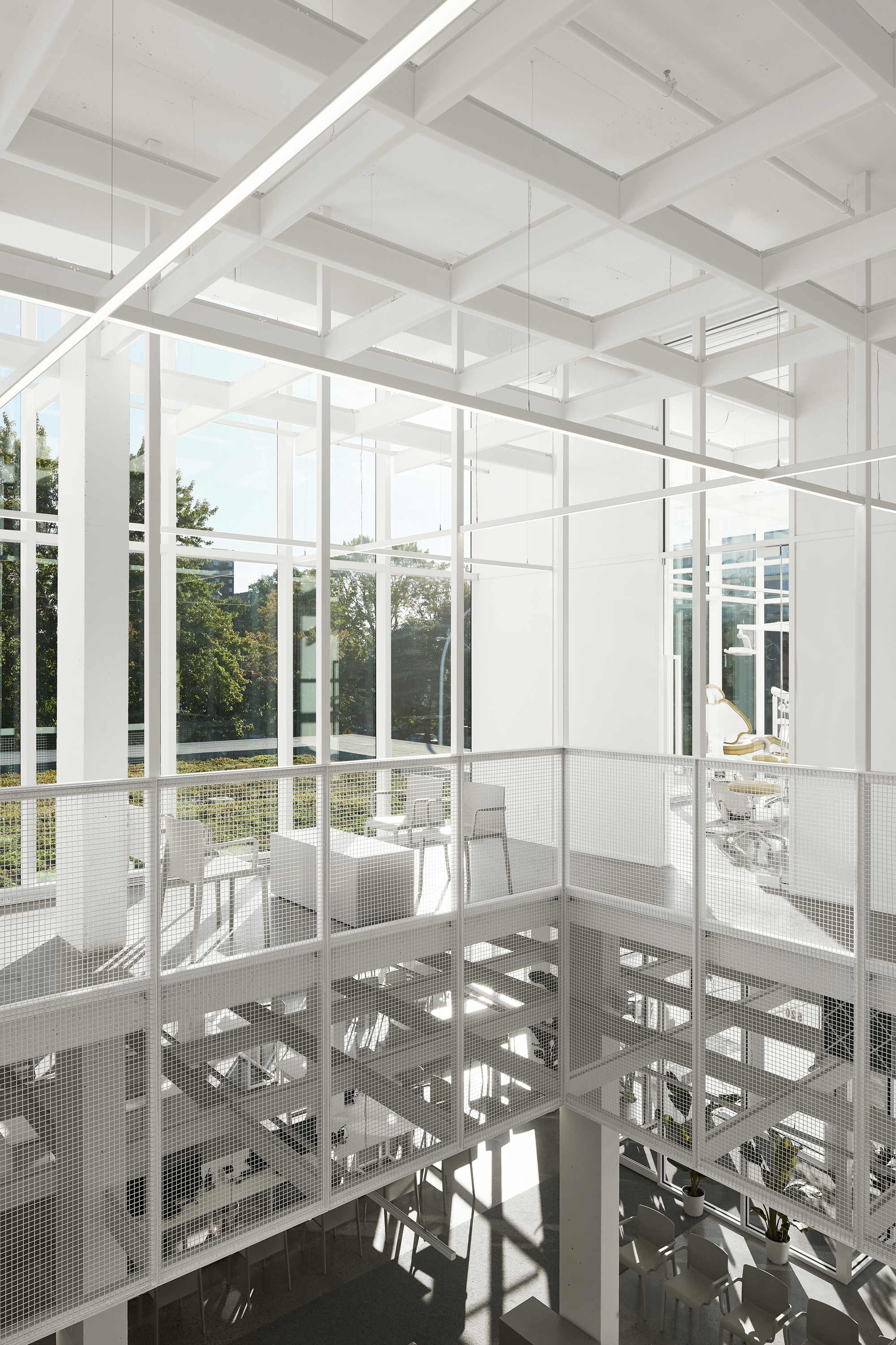 White steel framework and perforated metal mezzanine floor with double-height glazed walls overlooking garden