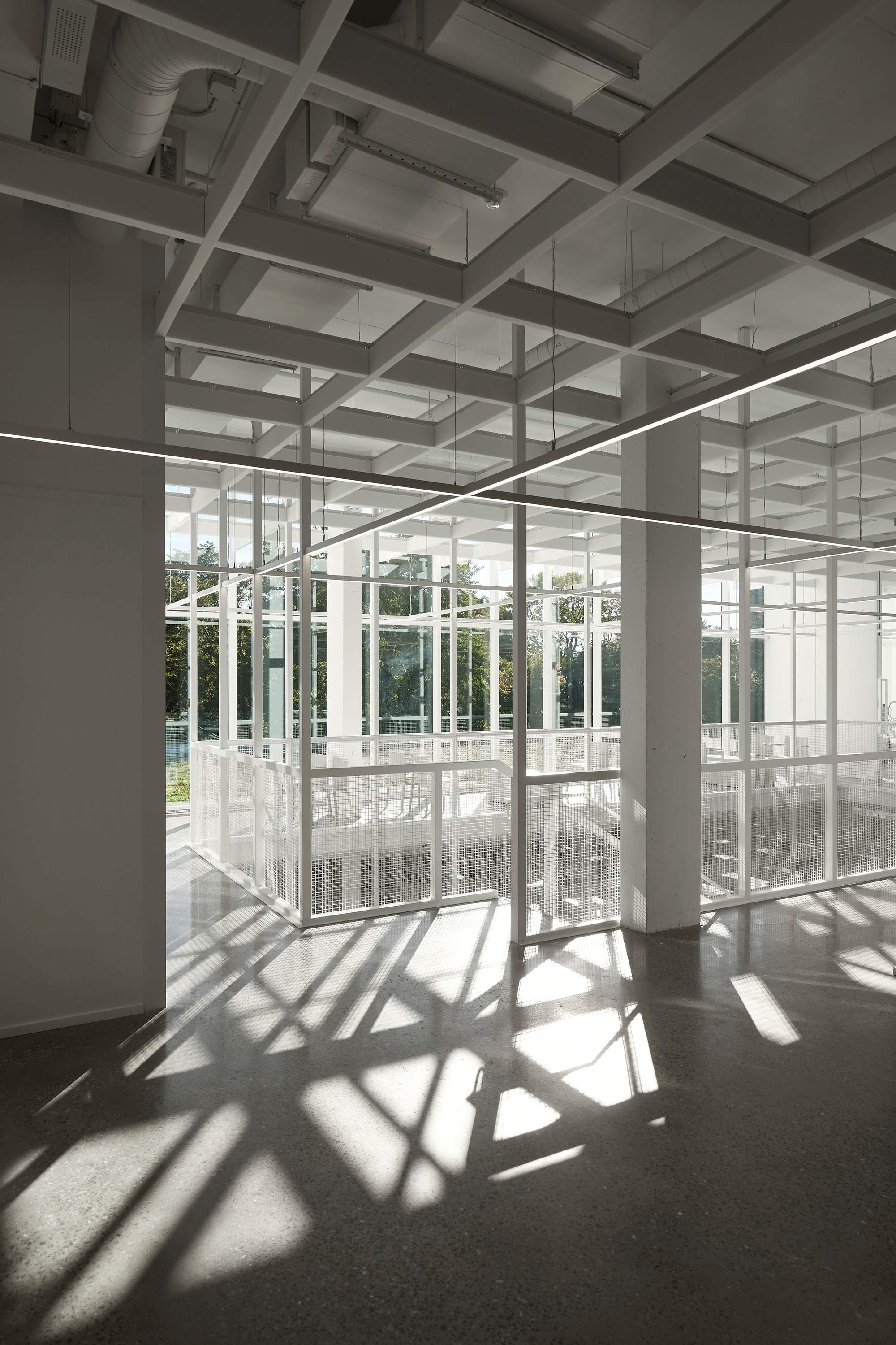 Polished concrete floor with geometric shadow patterns cast by structural frame and glazed enclosure