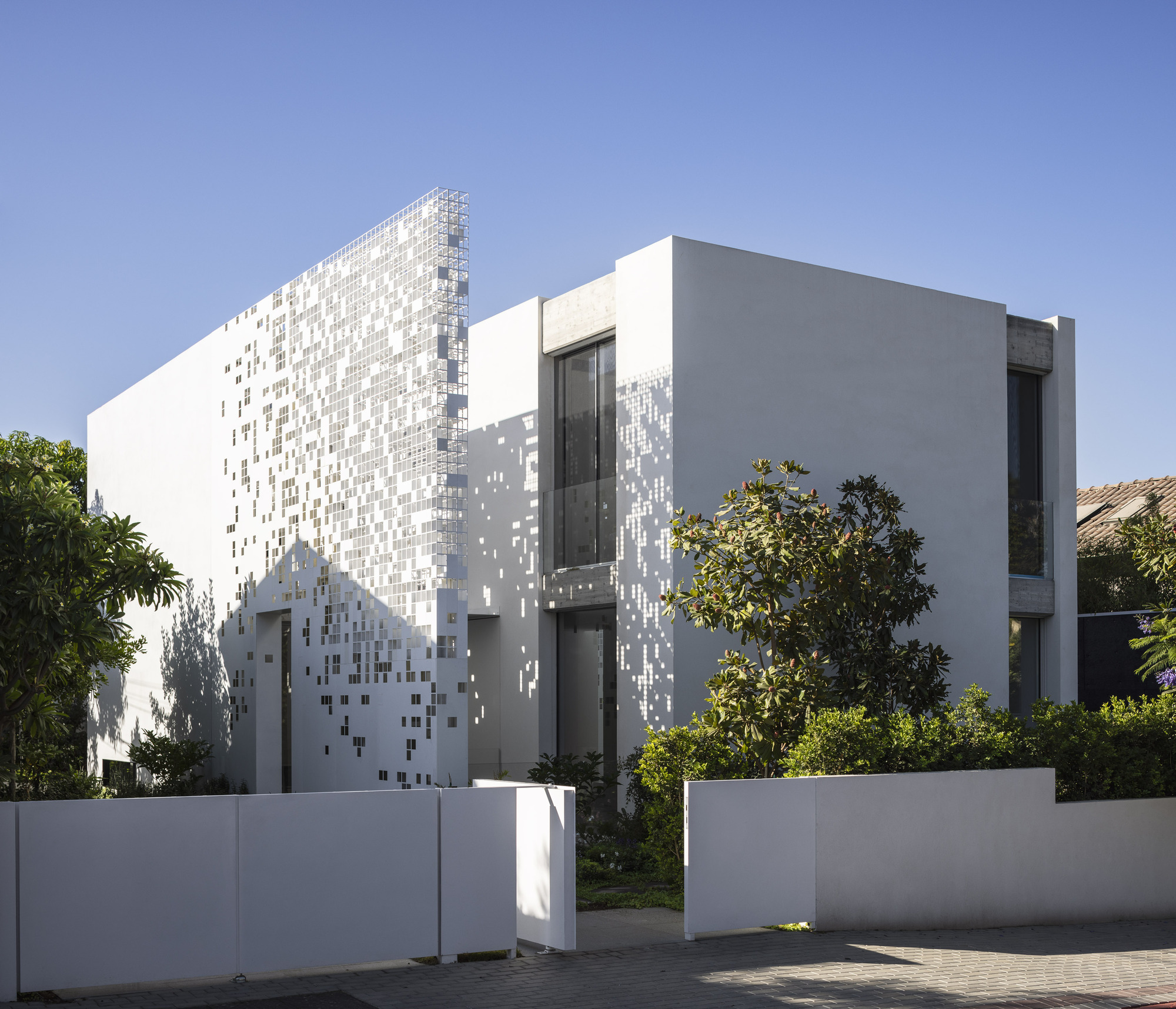 Street view of white volumes with pixelated tile screen and planted trees along pavement
