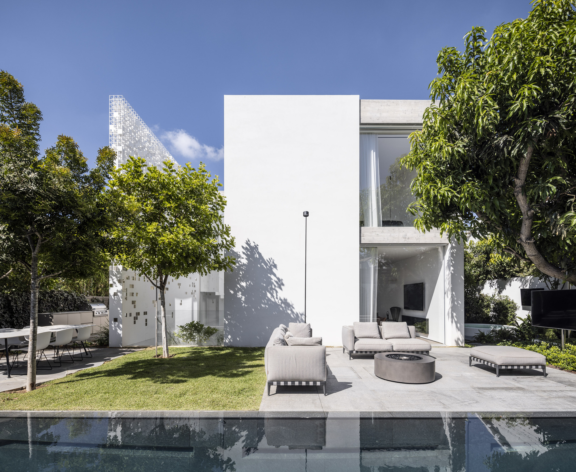 Pool terrace with white furniture and lawn beneath two-story glazed volume and pixelated screen