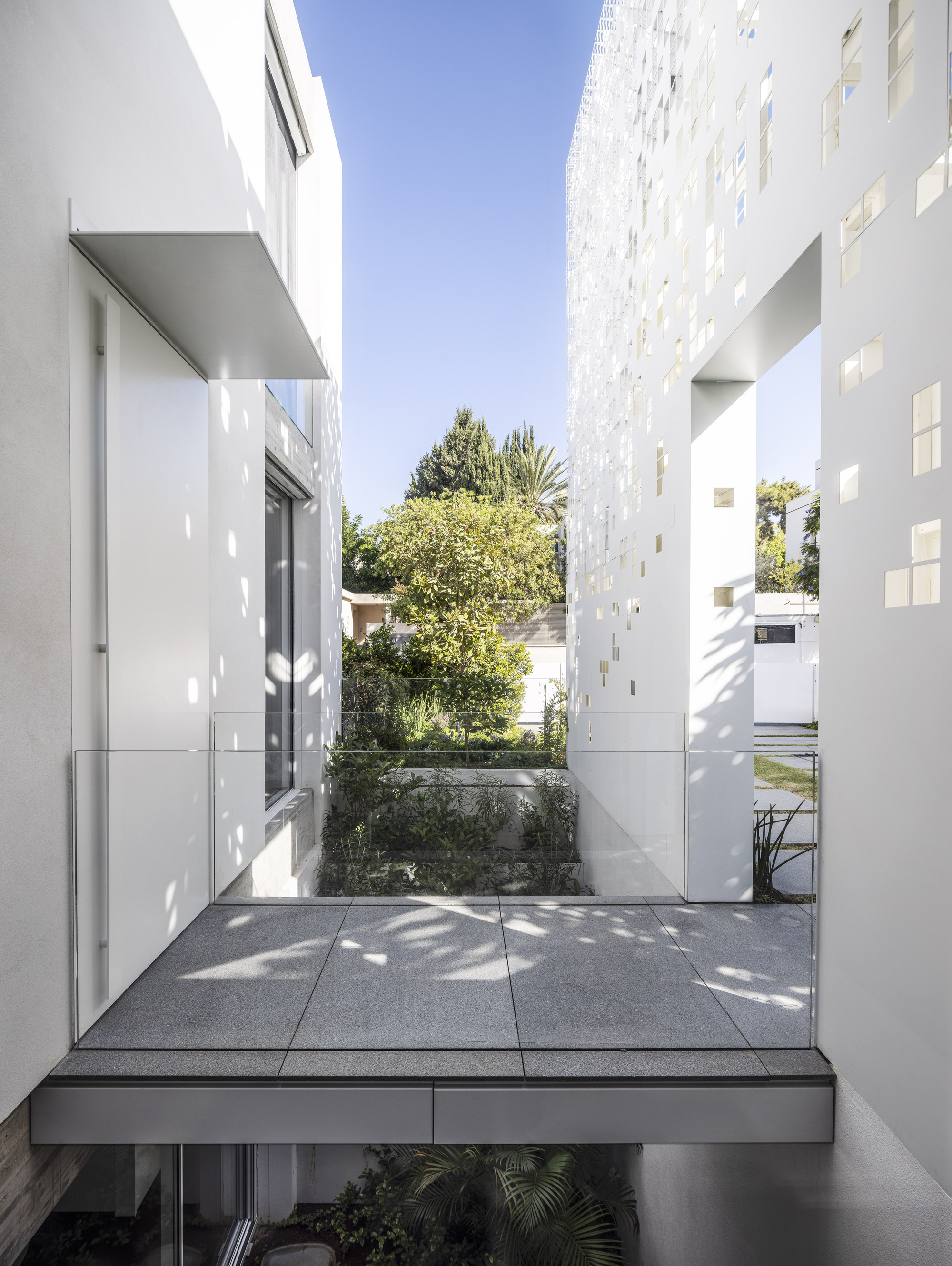 Terrazzo-paved terrace framed by white perforated screen walls with planted courtyard and dappled sunlight