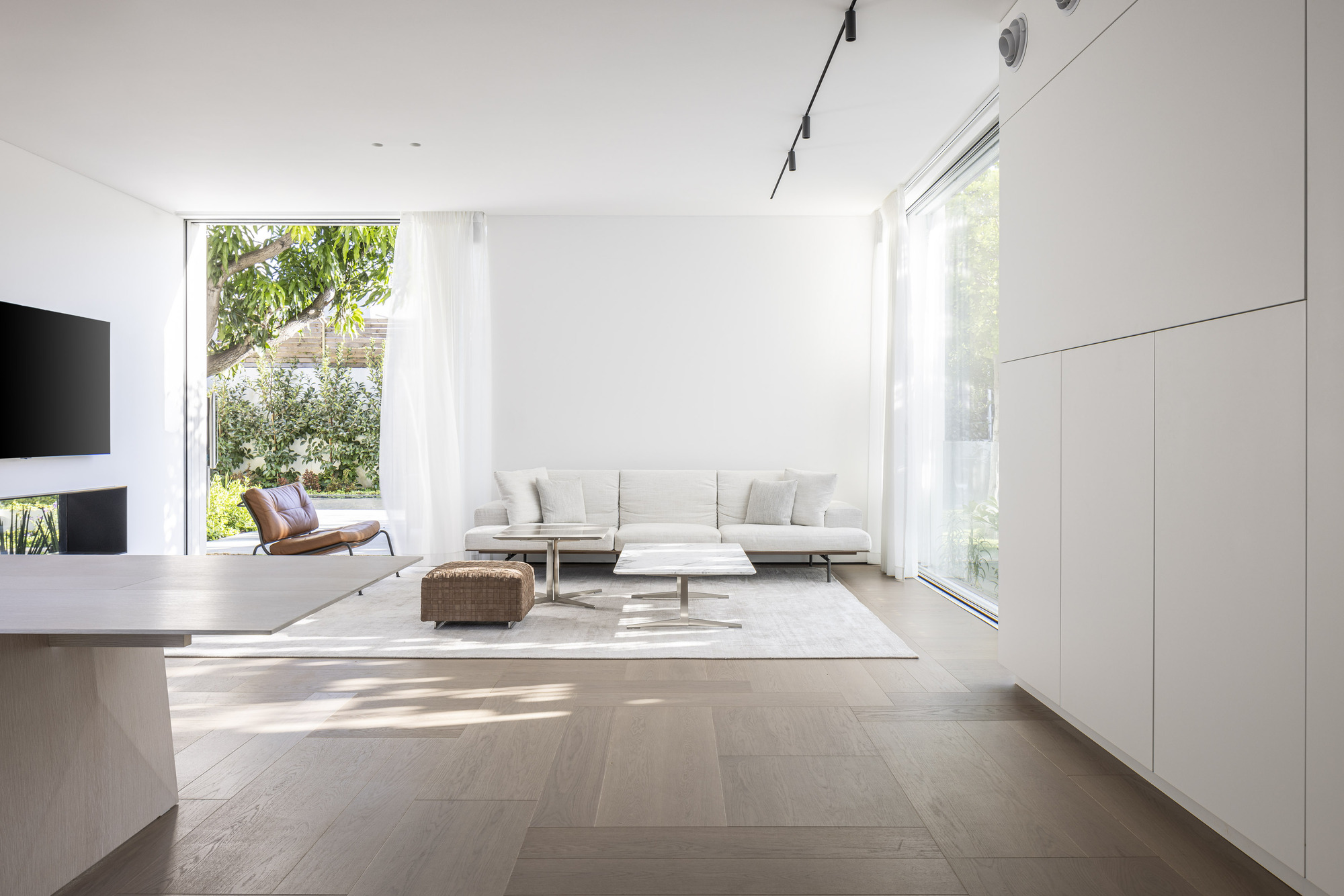 Open living room with wide plank oak flooring and floor-to-ceiling glazing overlooking garden greenery