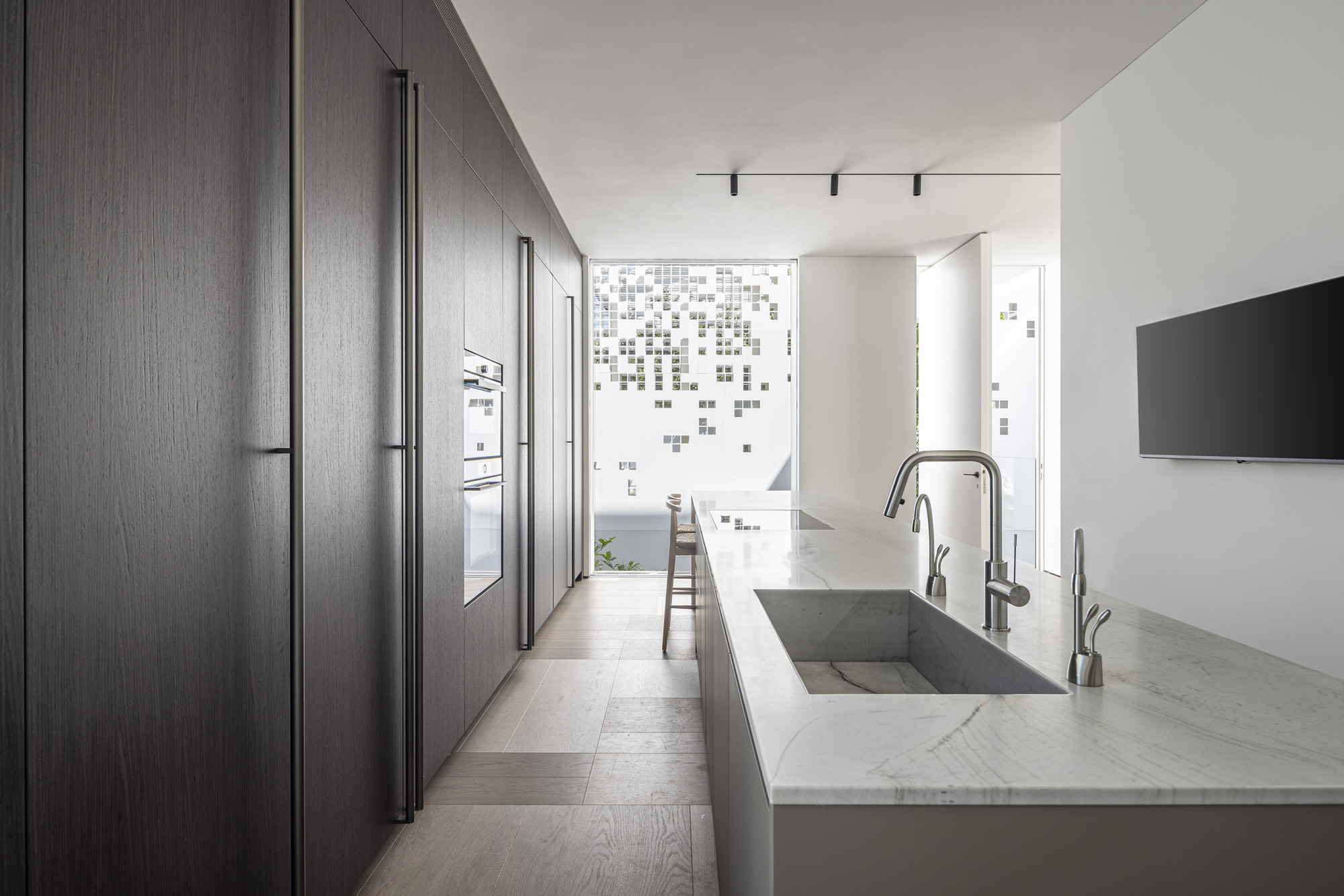Galley kitchen with dark wood cabinetry and marble waterfall island facing perforated facade screen
