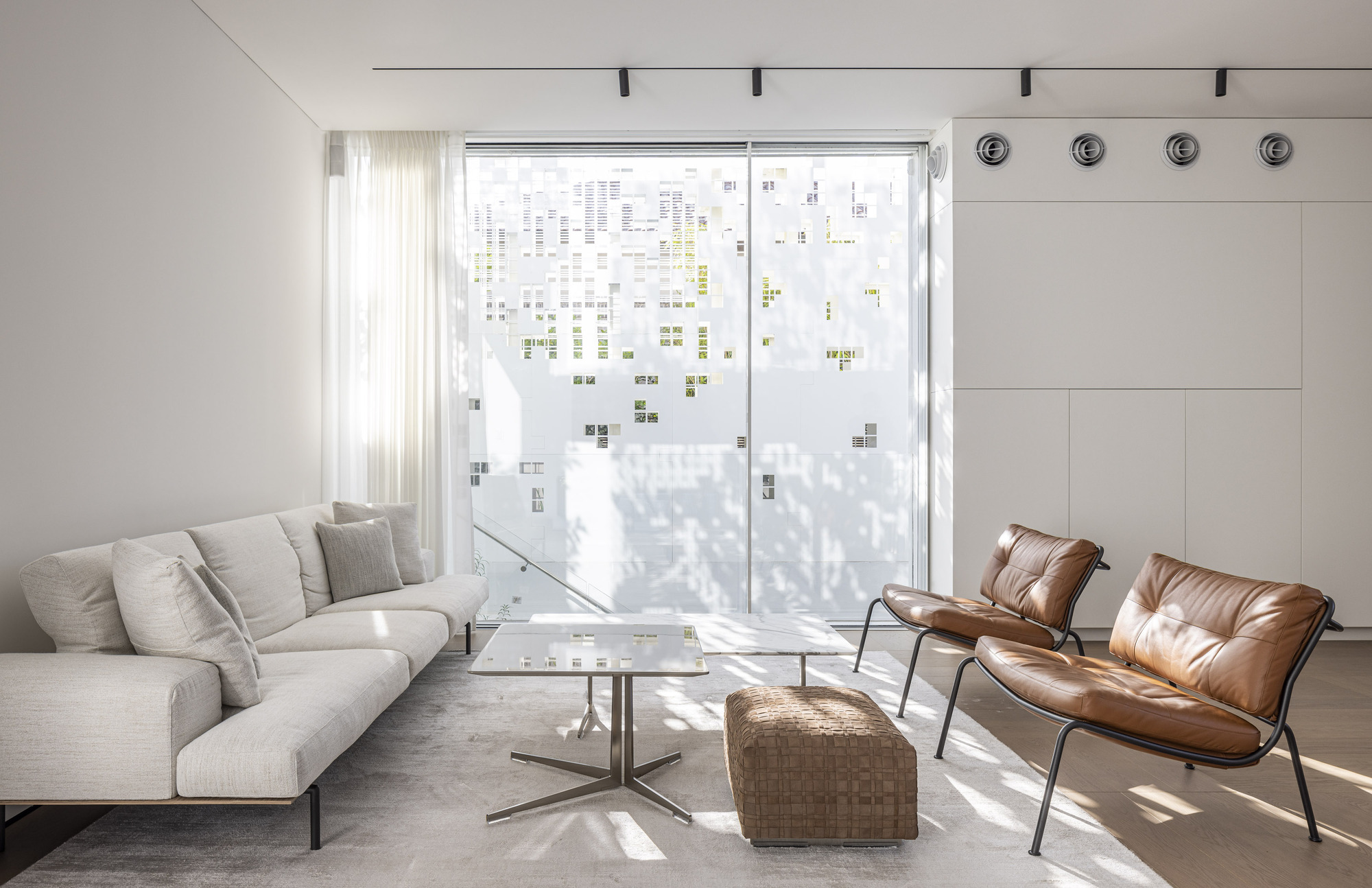 Living area with patterned perforated facade casting filtered shadows across seating and polished concrete floor