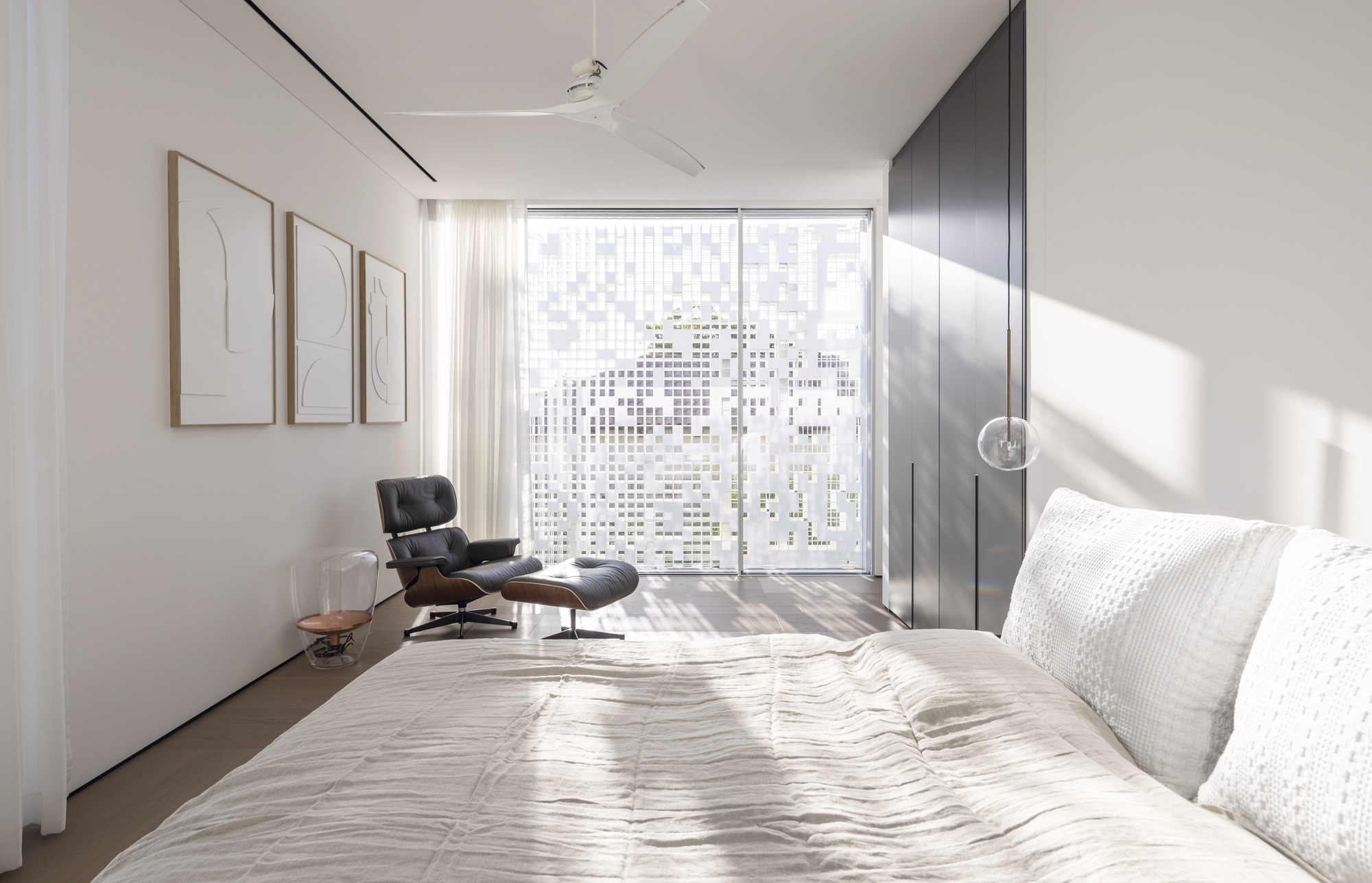 Bedroom with glazed wall behind dark timber wardrobe panels and afternoon light striping the floor