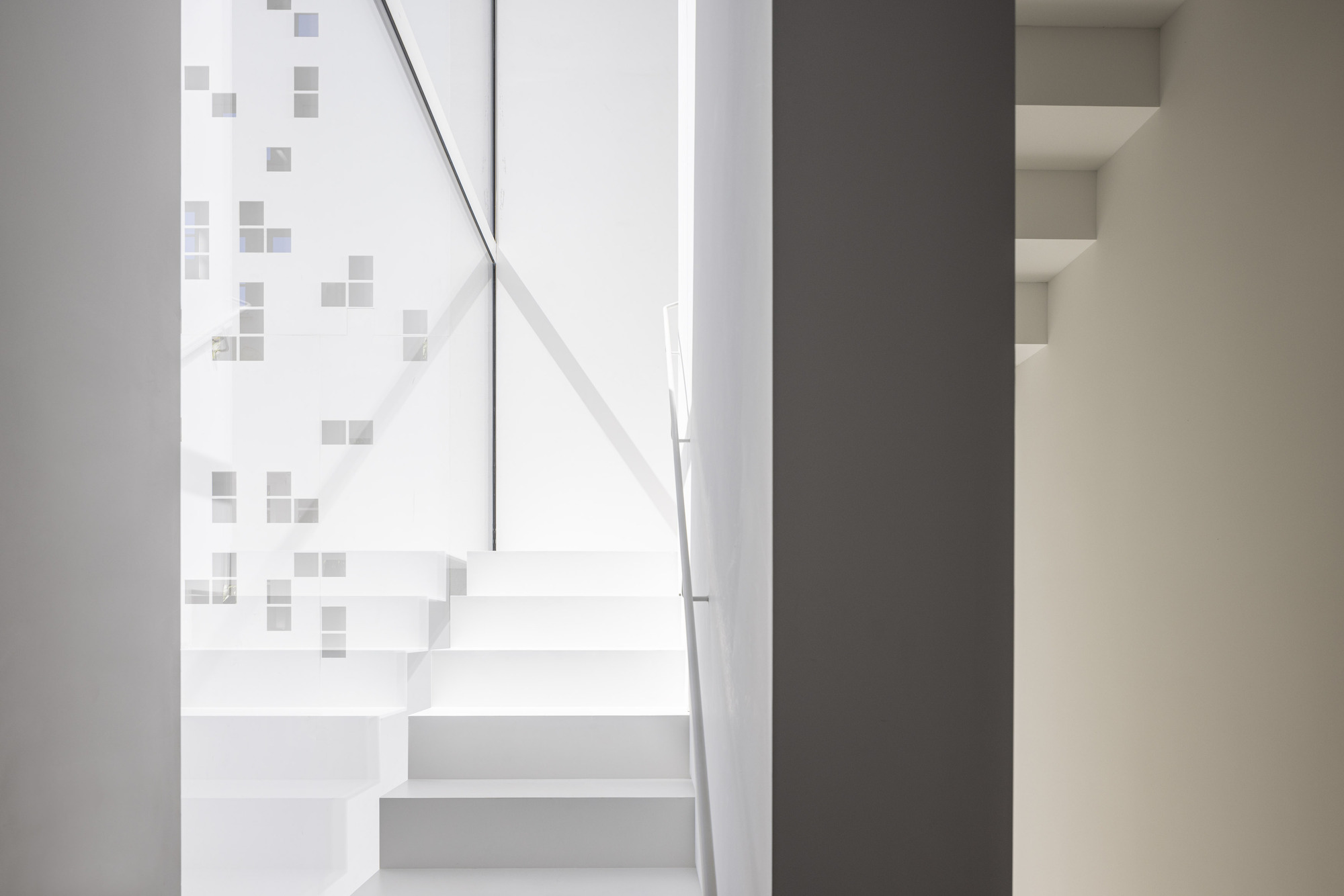 White floating staircase with metal handrail beside a wall with scattered square grey tiles