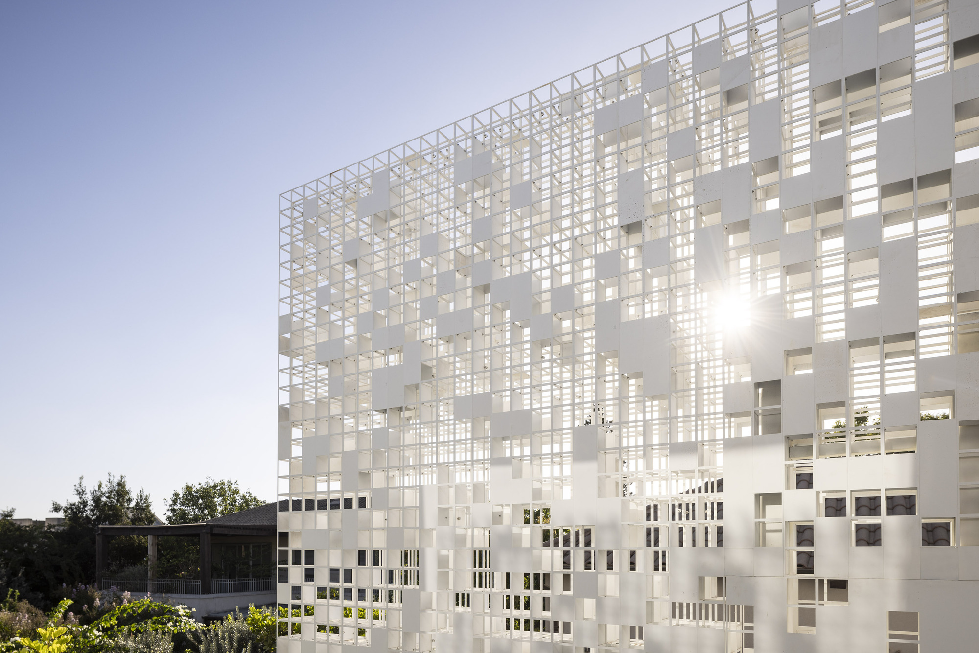 Perforated white screen facade at dusk with warm interior lighting glowing through the openings