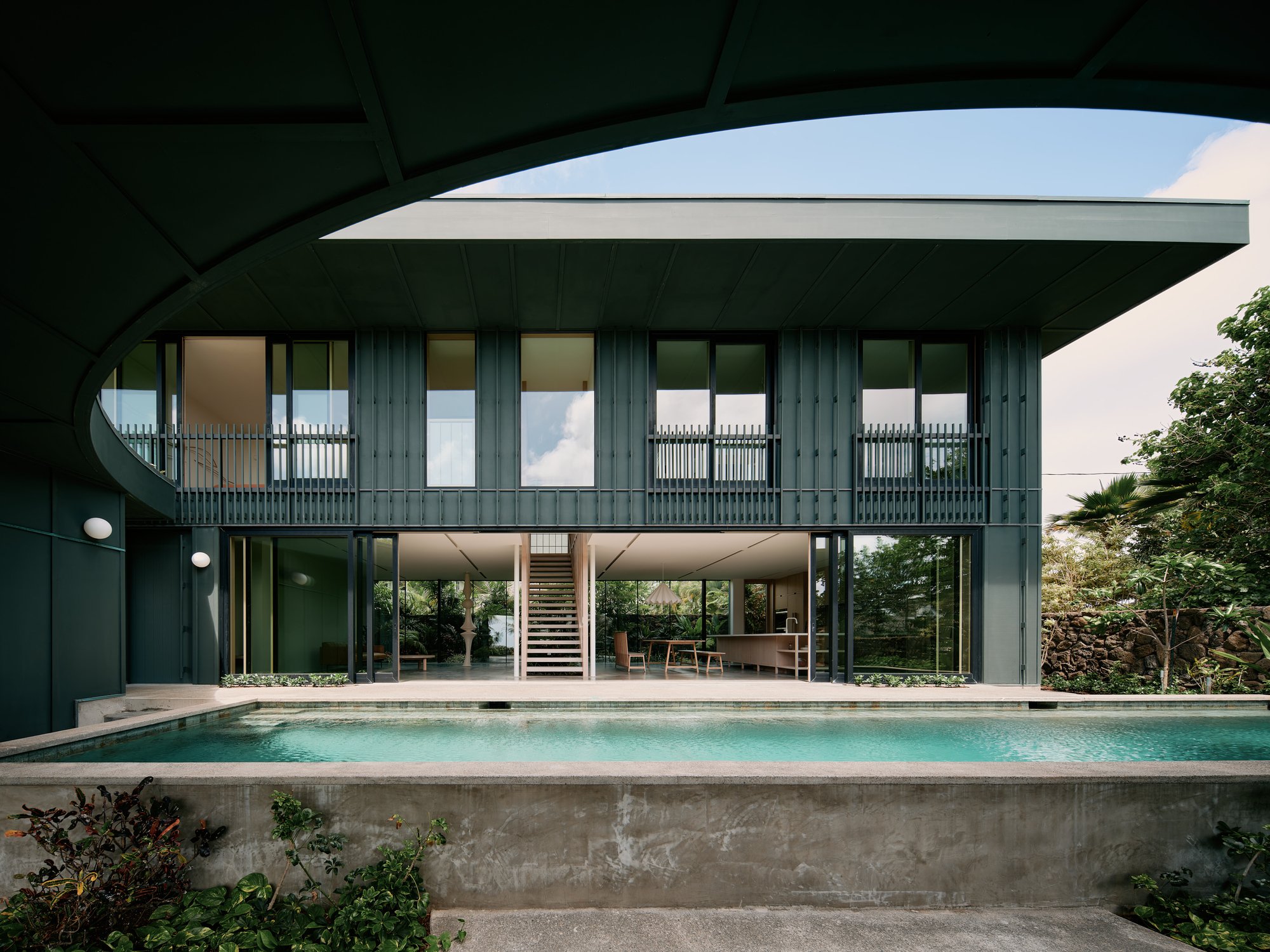 Rear facade with dark vertical cladding and open ground floor overlooking the elevated concrete lap pool