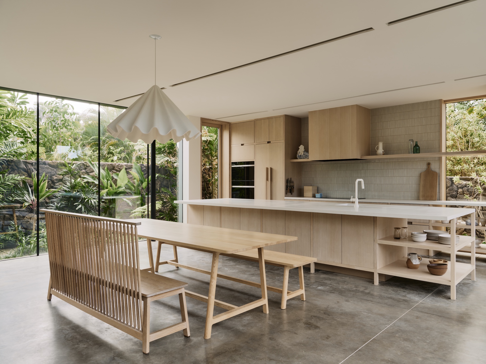 Kitchen island with timber bench seating and pendant light beside floor-to-ceiling glazing overlooking garden
