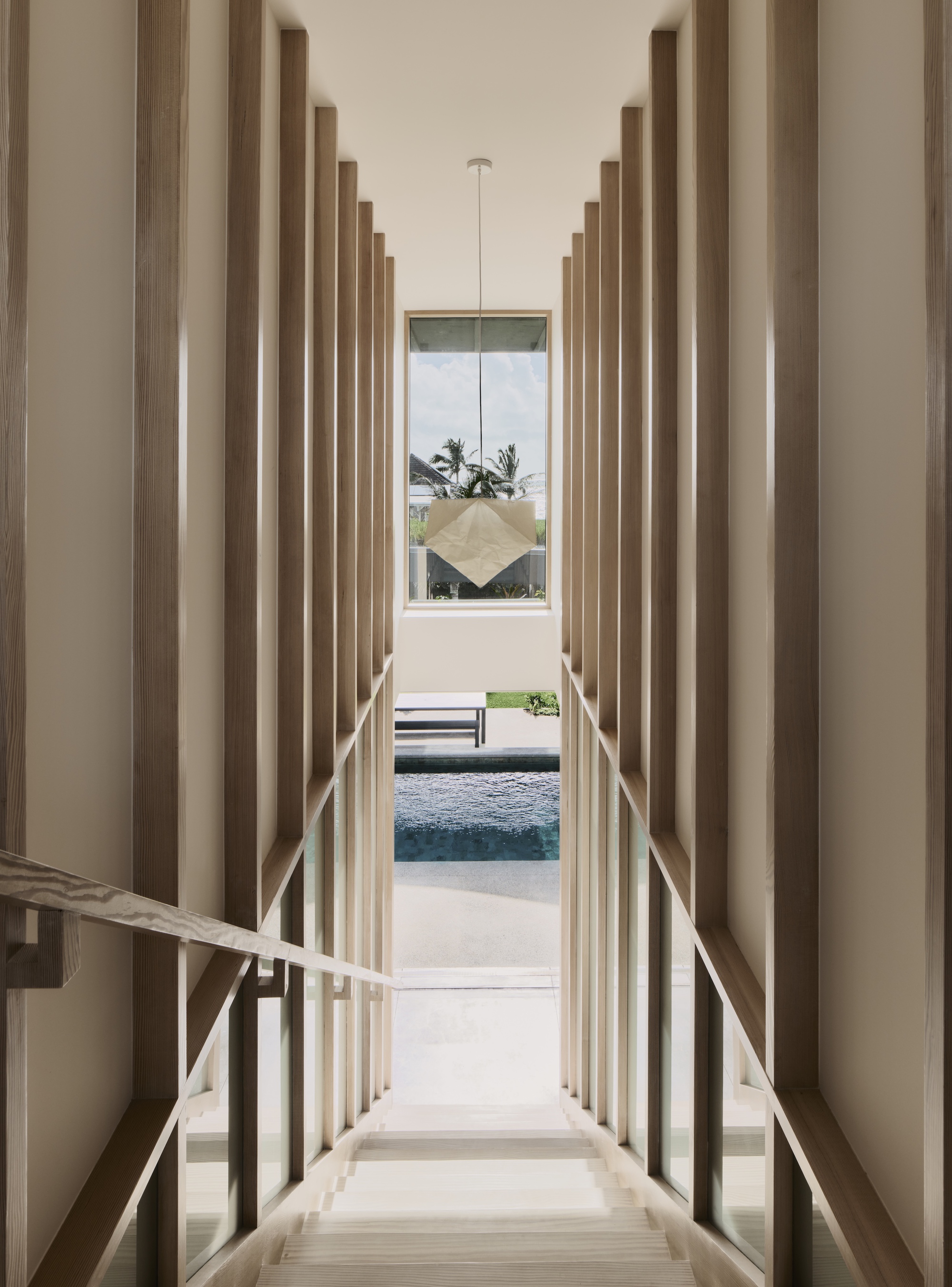 Descending staircase framed by vertical timber battens with view to pool and palms beyond