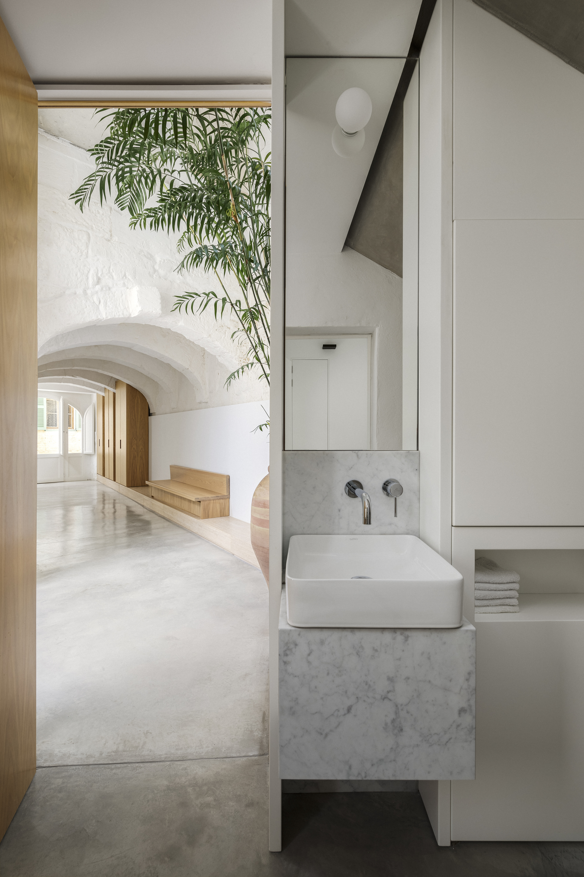 Bathroom with floating marble sink beneath an arched corridor and overhanging palm fronds