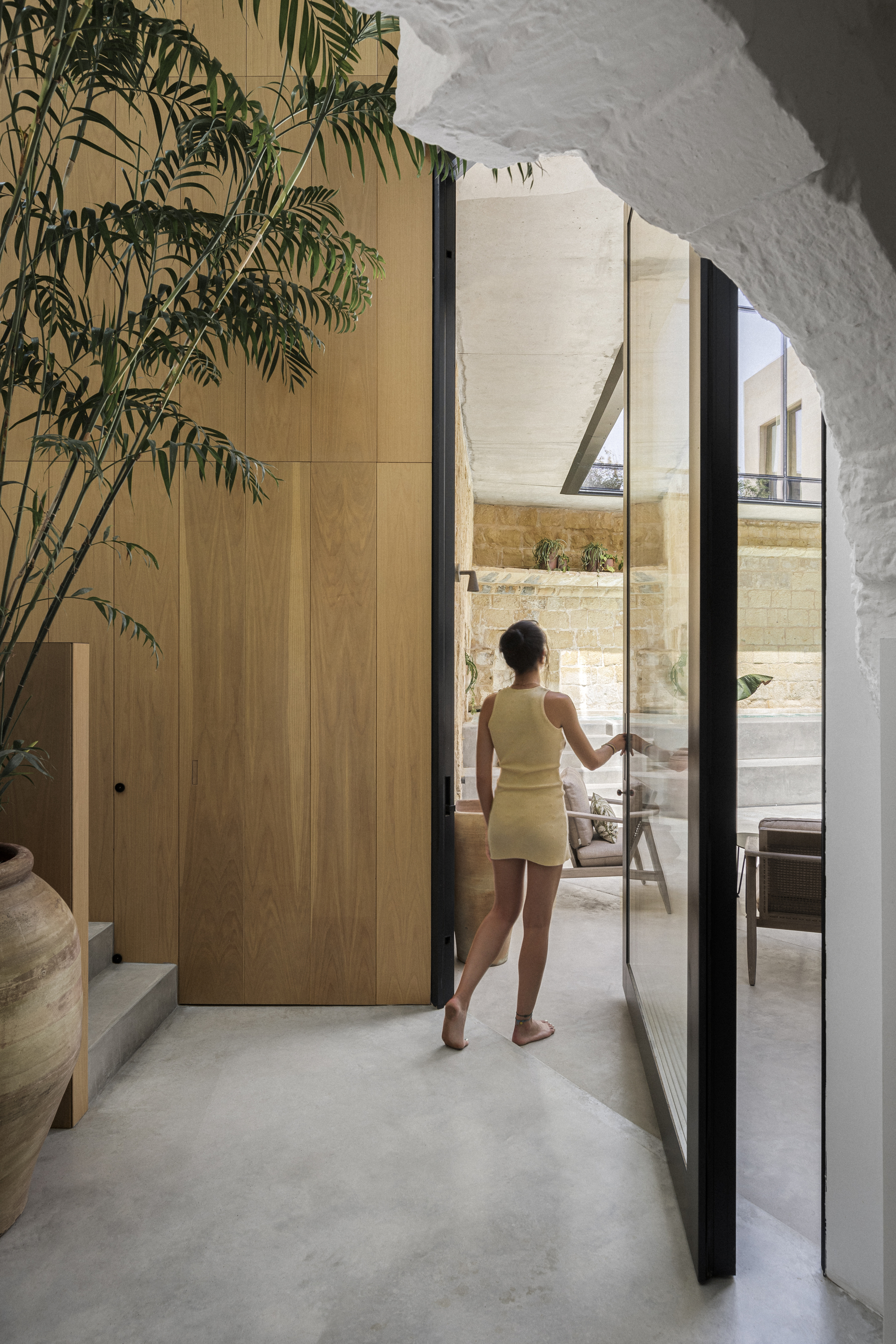 Woman opening glass door to courtyard from timber-clad hallway with potted palm