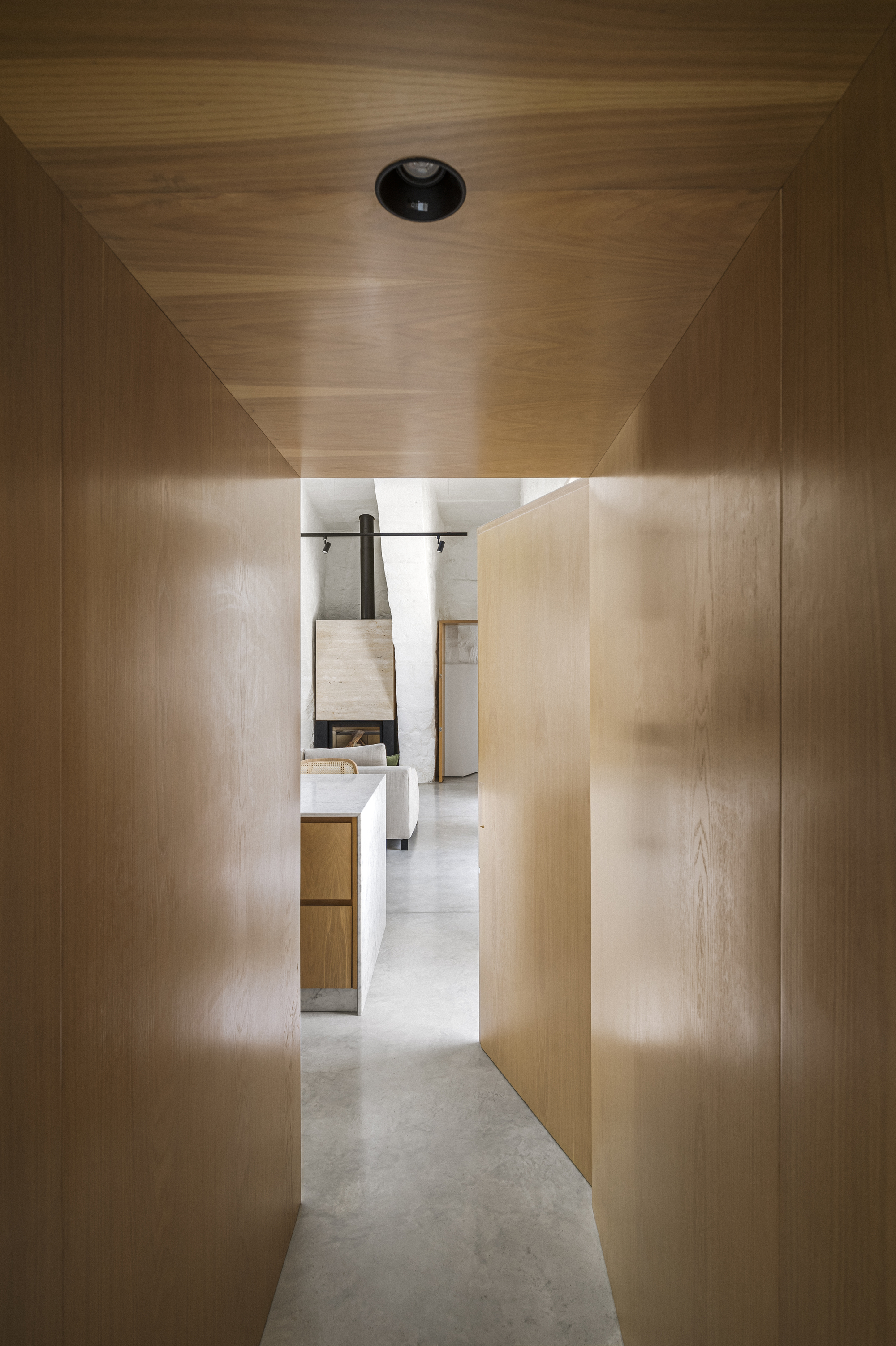 Timber-clad corridor with backlit translucent panels leading toward bathroom at the end