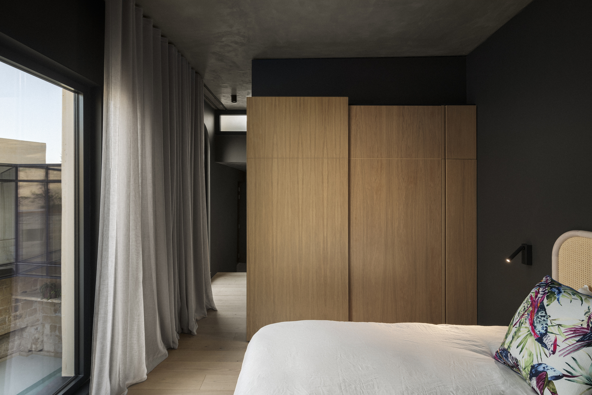 Bedroom with oak wardrobe panels, grey curtains and exposed concrete ceiling