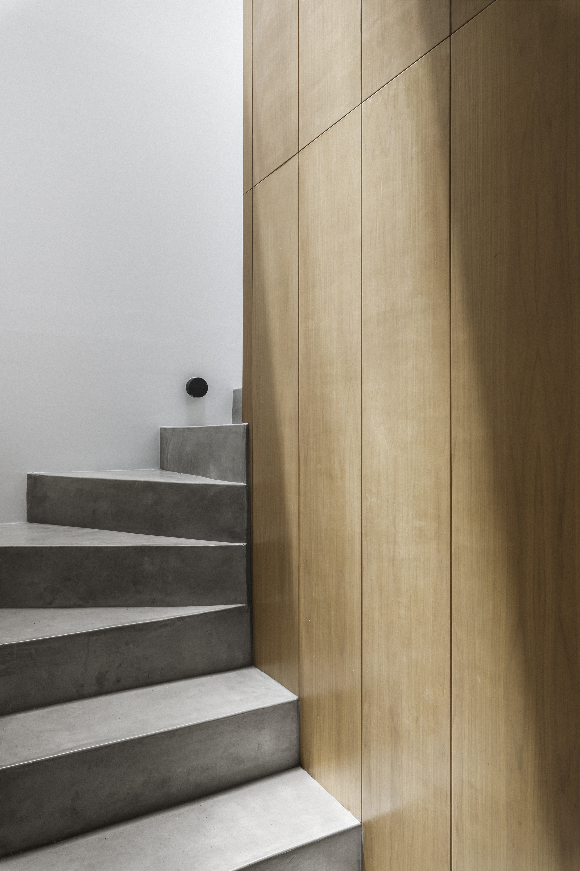 Concrete staircase with white risers meeting a vertical oak paneled wall