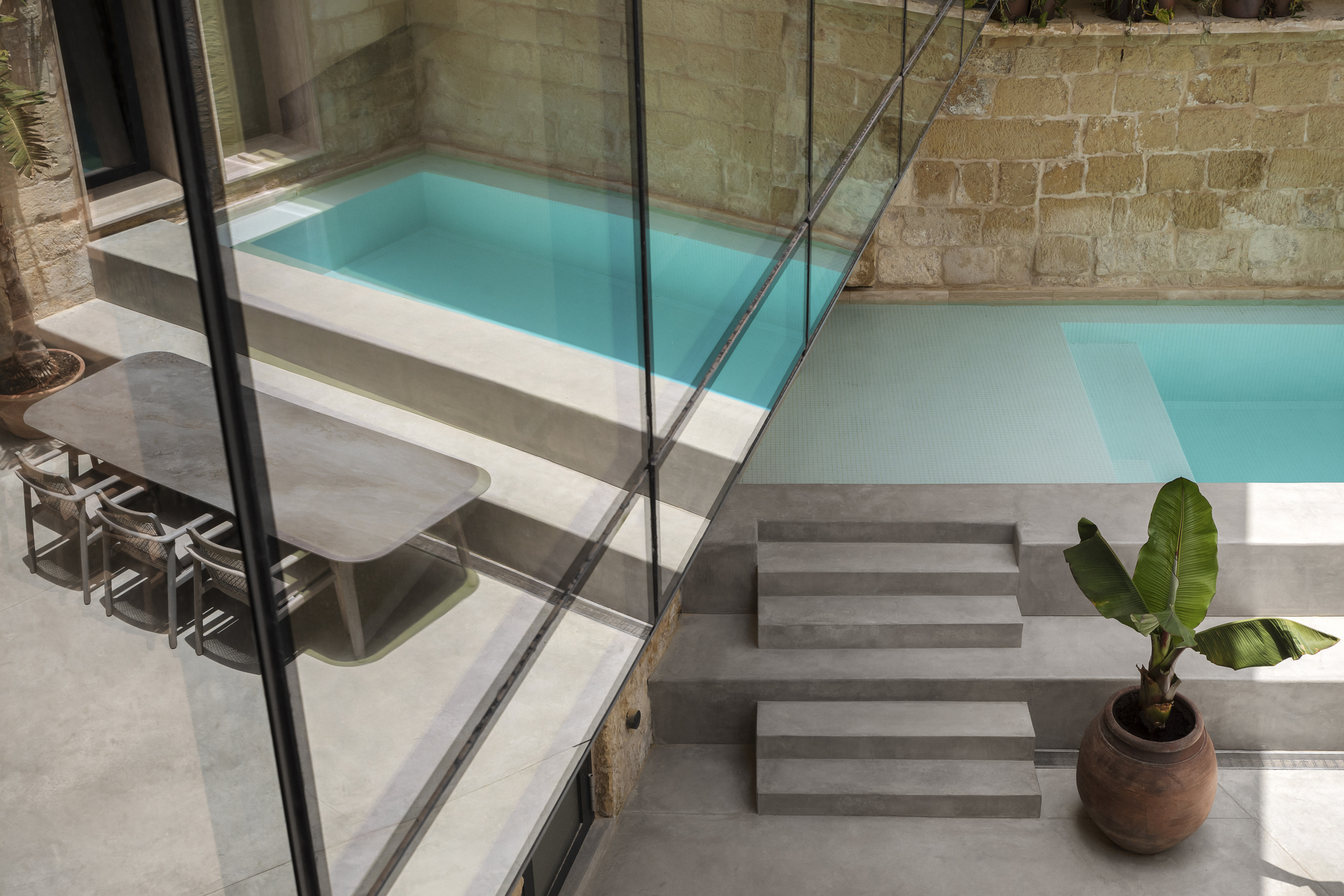 Swimming pool terrace with glass balustrade, concrete steps and potted banana plant