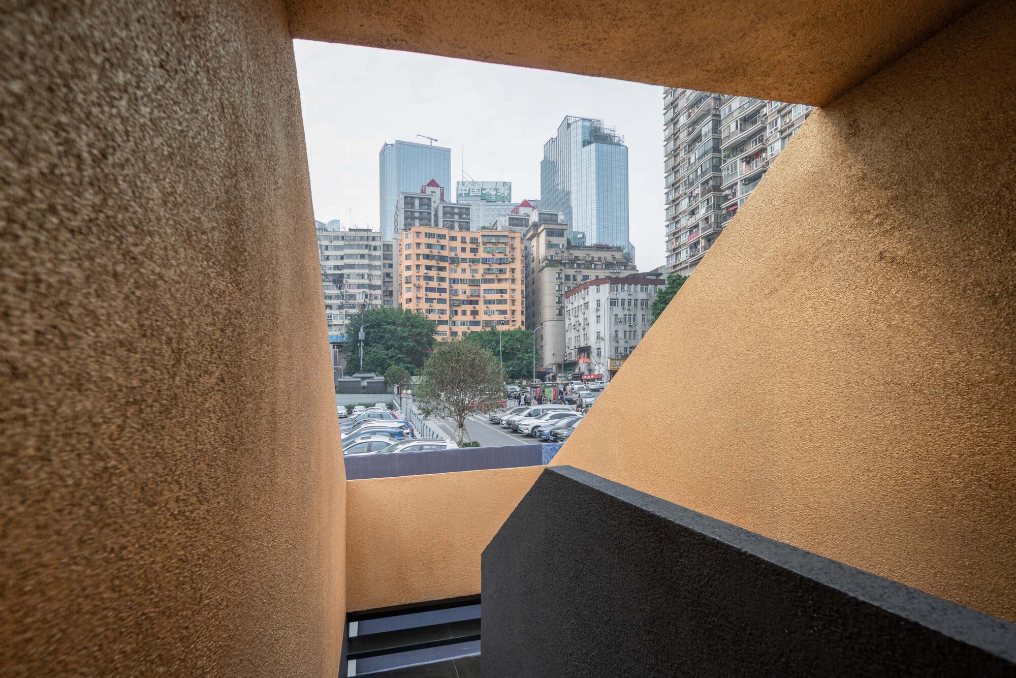 Triangular window opening framing the urban skyline beyond the textured ochre interior walls
