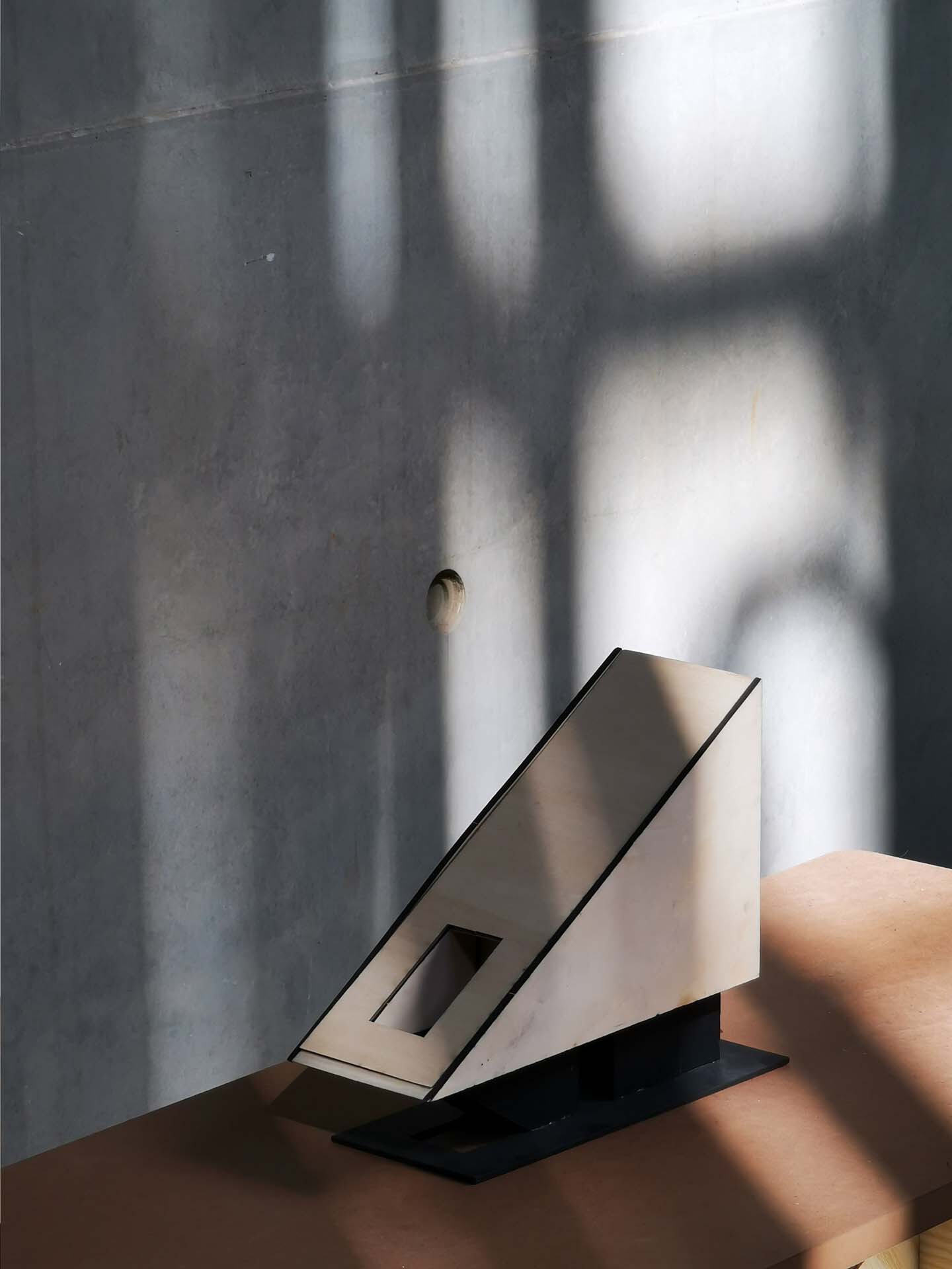 Angular white stair section beside a polished grey concrete wall with soft window shadows