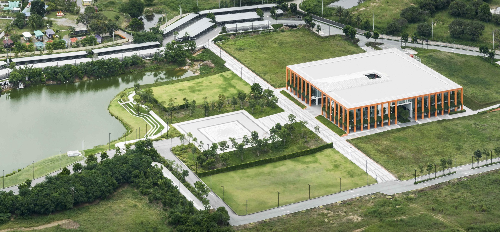 Aerial view of the complex with vertical timber facade, green roofs, and adjacent pond