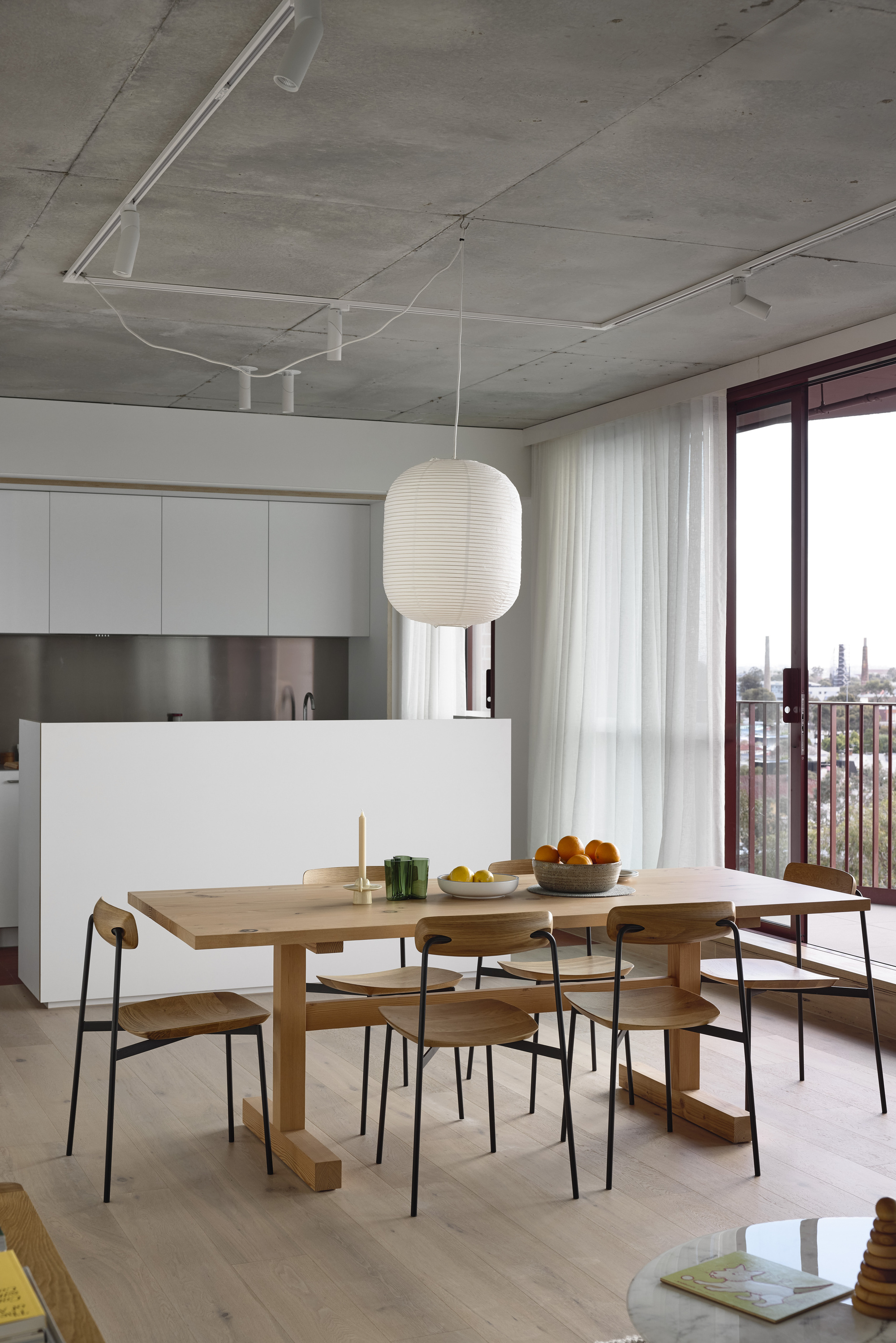 Open kitchen and dining area with exposed concrete ceiling and sheer curtains at the balcony door