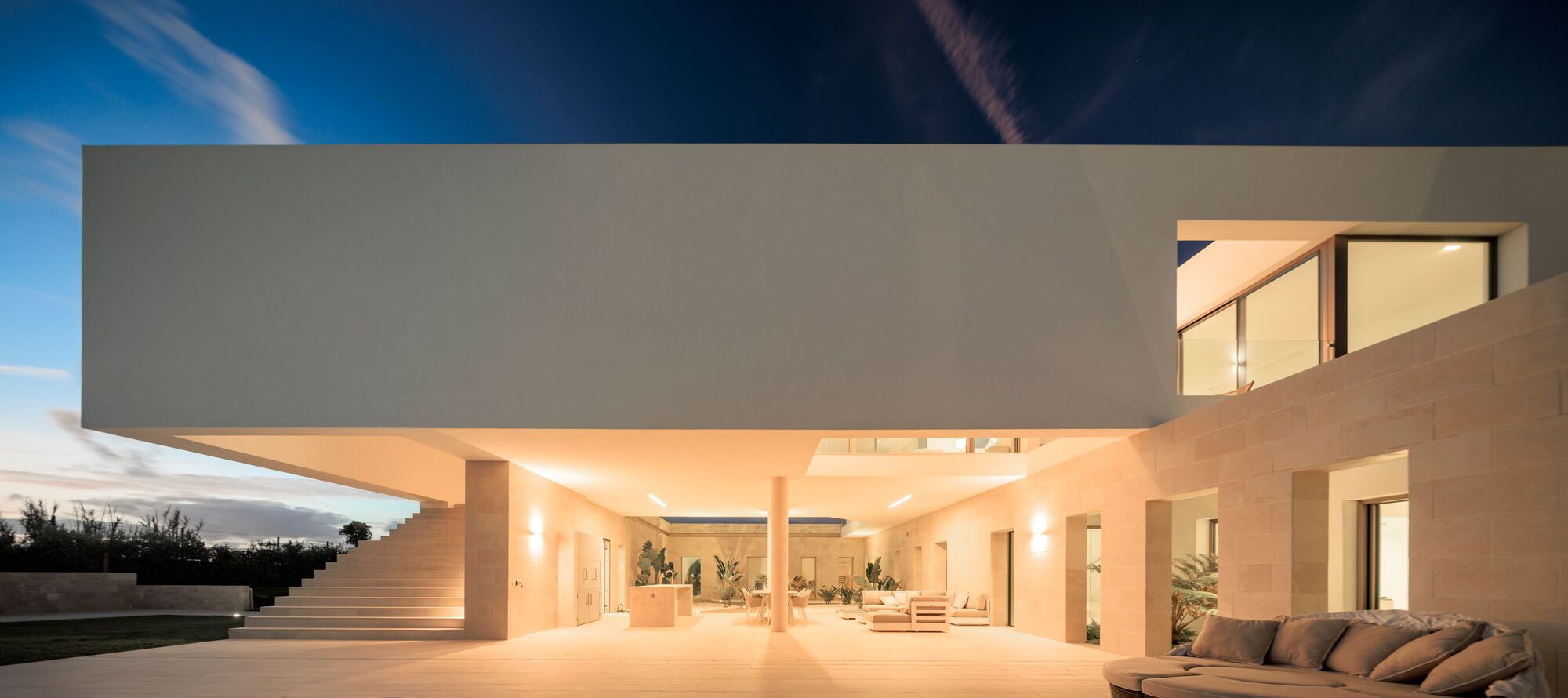 Exterior terrace with cantilevered volume above illuminated open-air living space at dusk