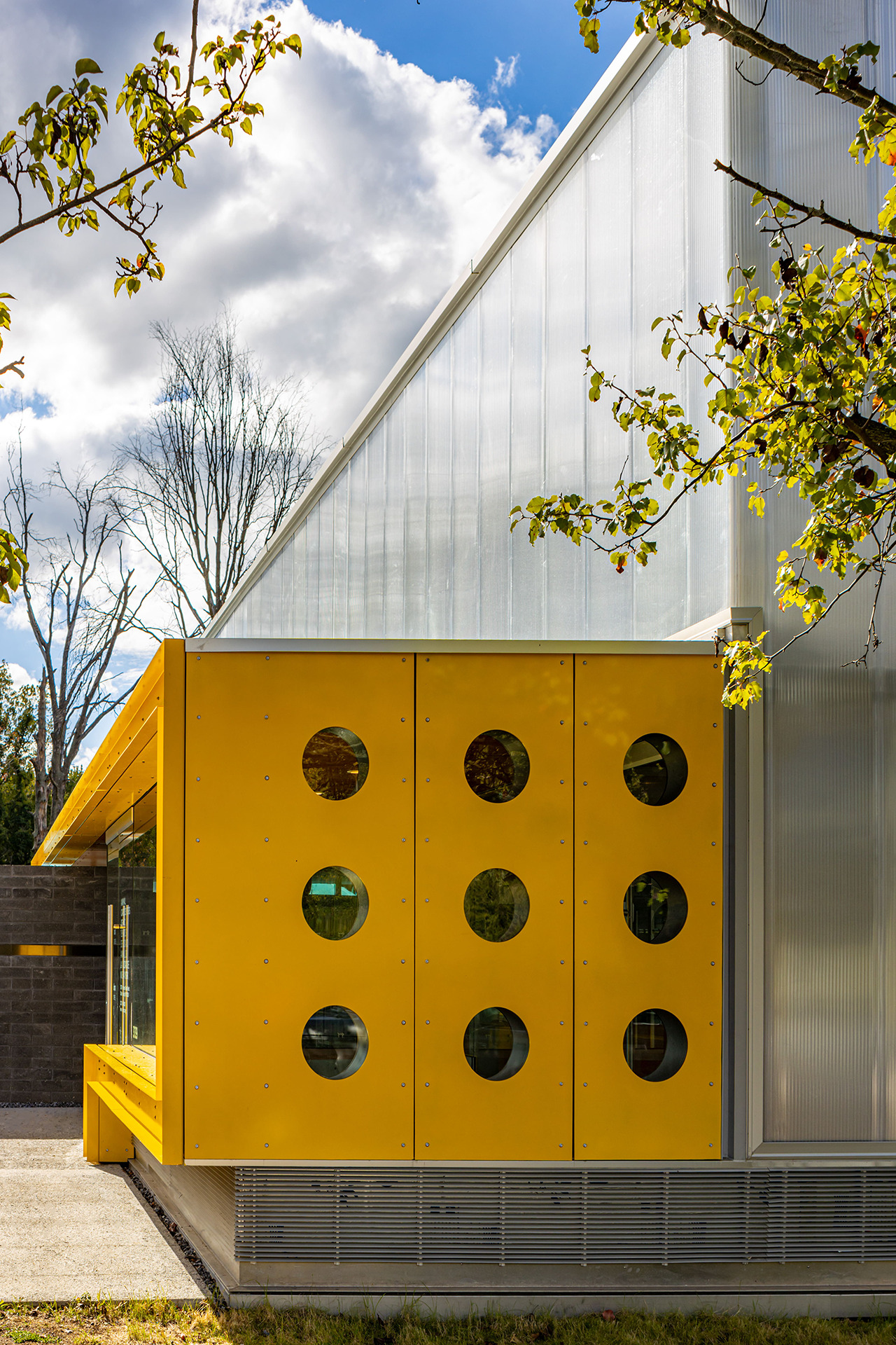 Yellow facade with nine circular porthole windows beneath sloped translucent polycarbonate wall