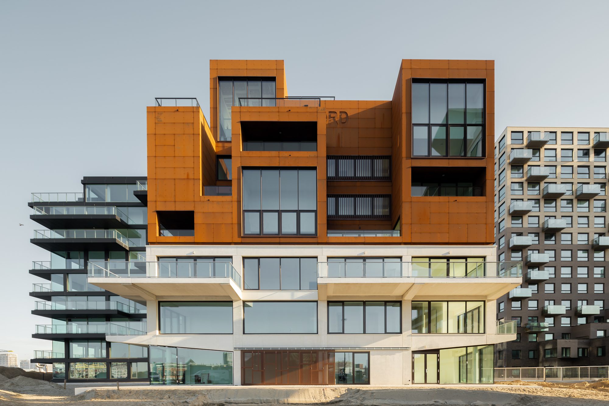 Street-level view of the articulated base with cor-ten steel volumes above white ground floor units