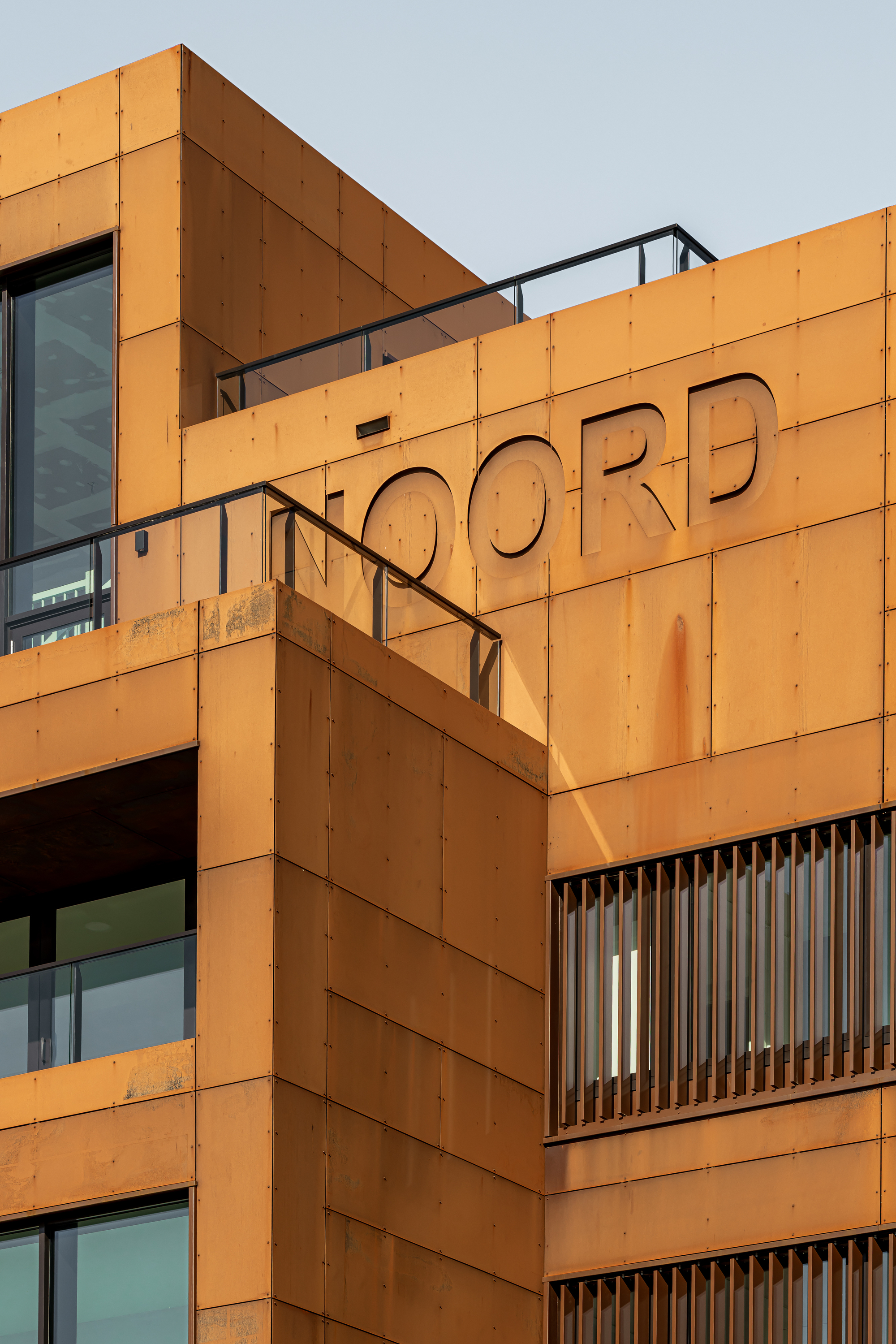Close-up of orange-cladded facade with cut-out lettering and vertical slat screening at dusk
