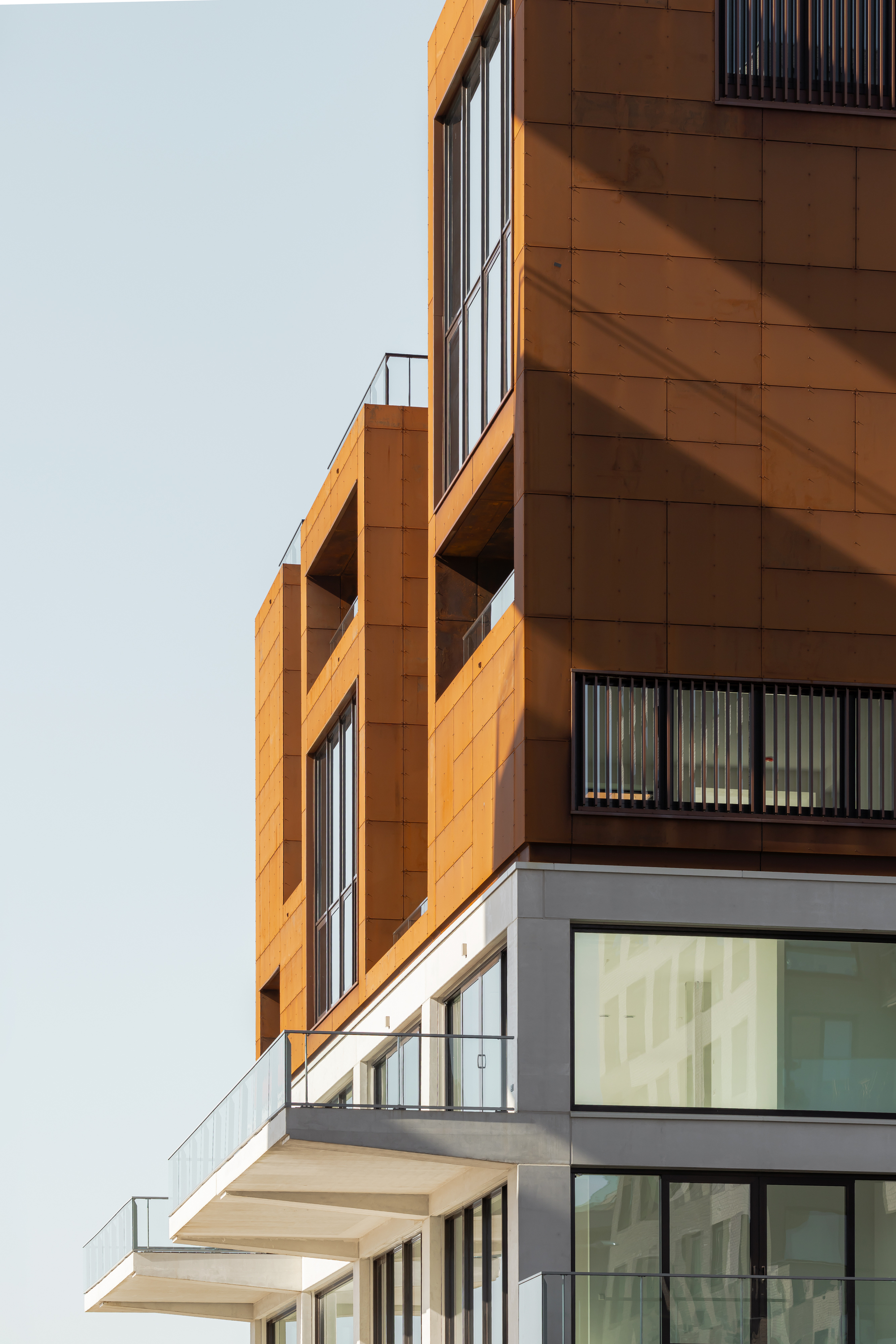 Stacked balconies with cantilevered orange panels and glass railings against a clear sky