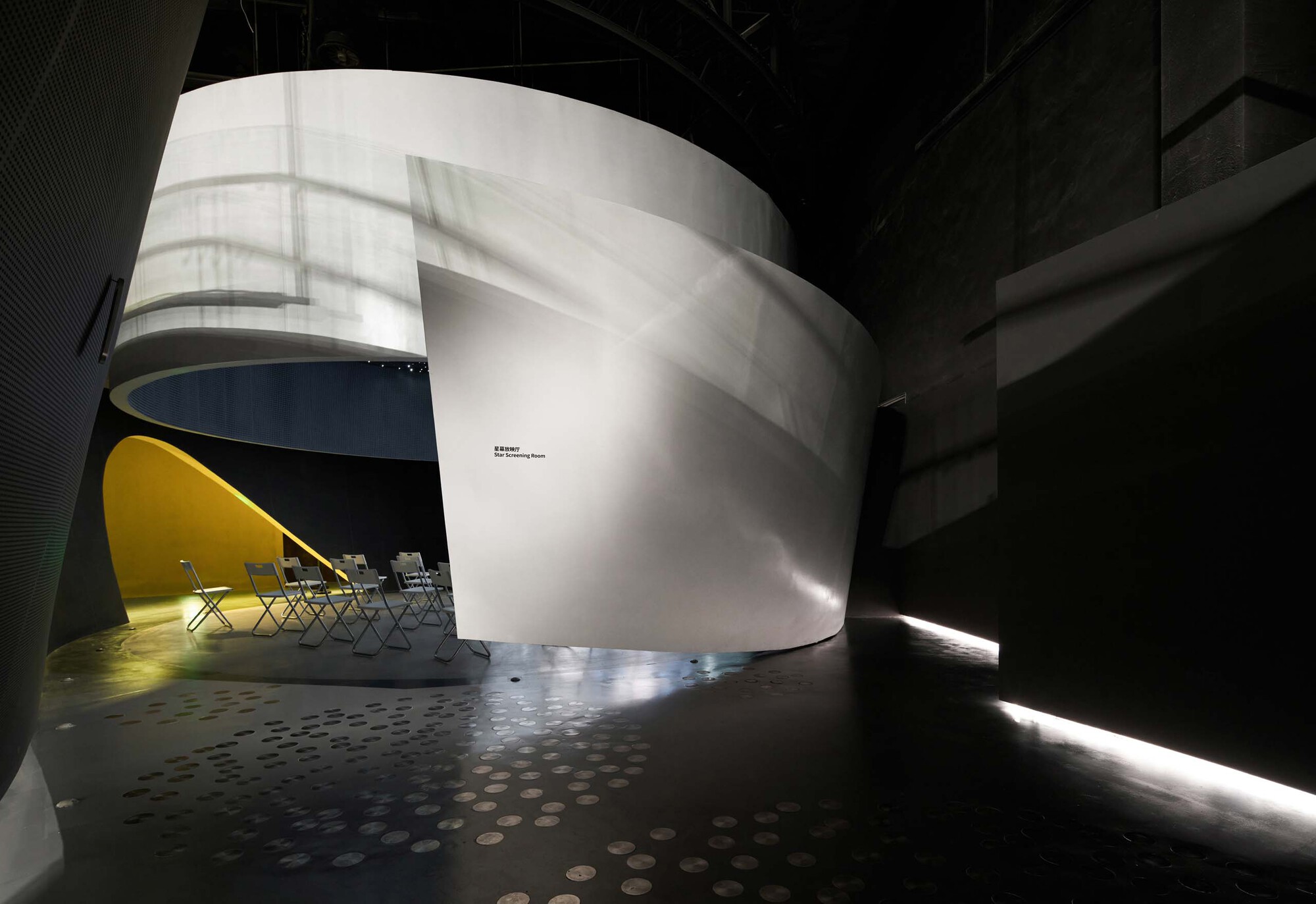 Curved white sculptural volume enclosing a seating area under exposed steel trusses