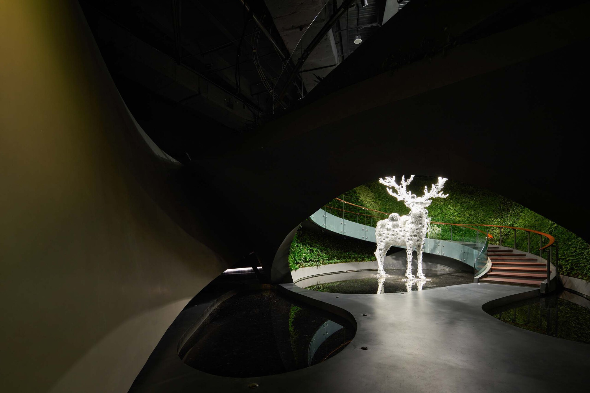 Interior view showing illuminated deer sculpture beside moss-covered walls and organic floor opening