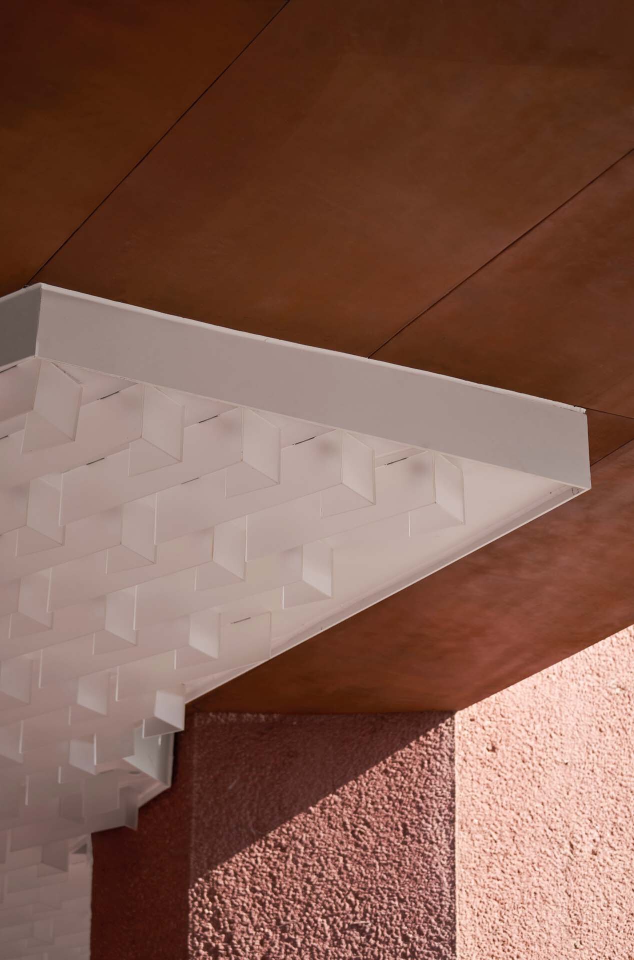 Detail of white three-dimensional coffered ceiling panel meeting a corten steel soffit and pink textured wall