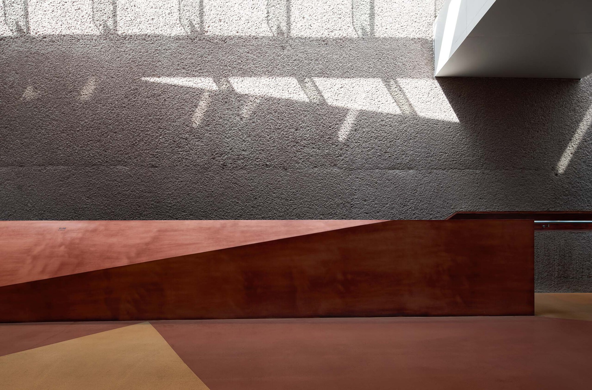 Intersection of corten steel plane and pink floor with patterned shadows from overhead screening