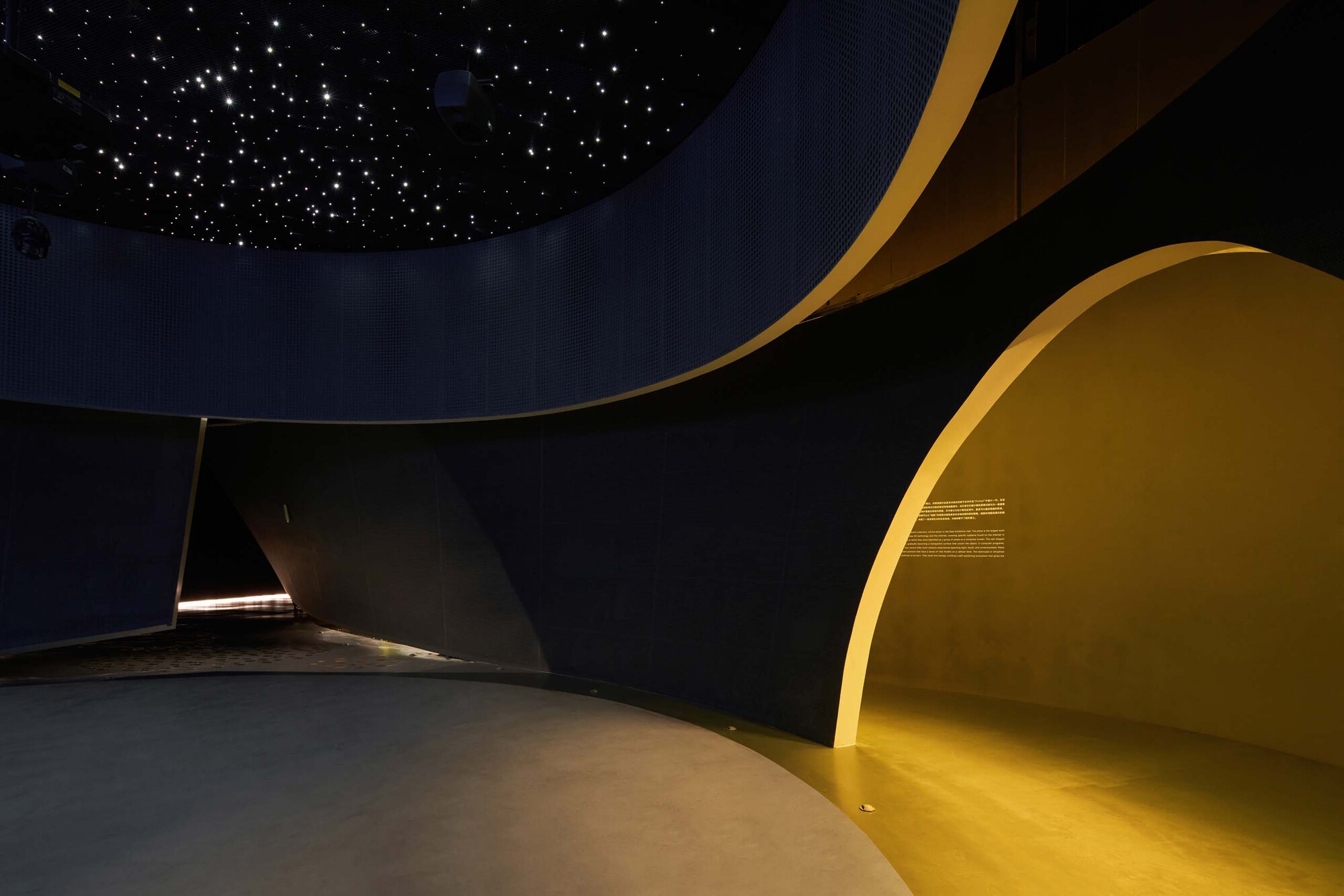 Curved interior wall with yellow illuminated alcove beneath a starlit ceiling