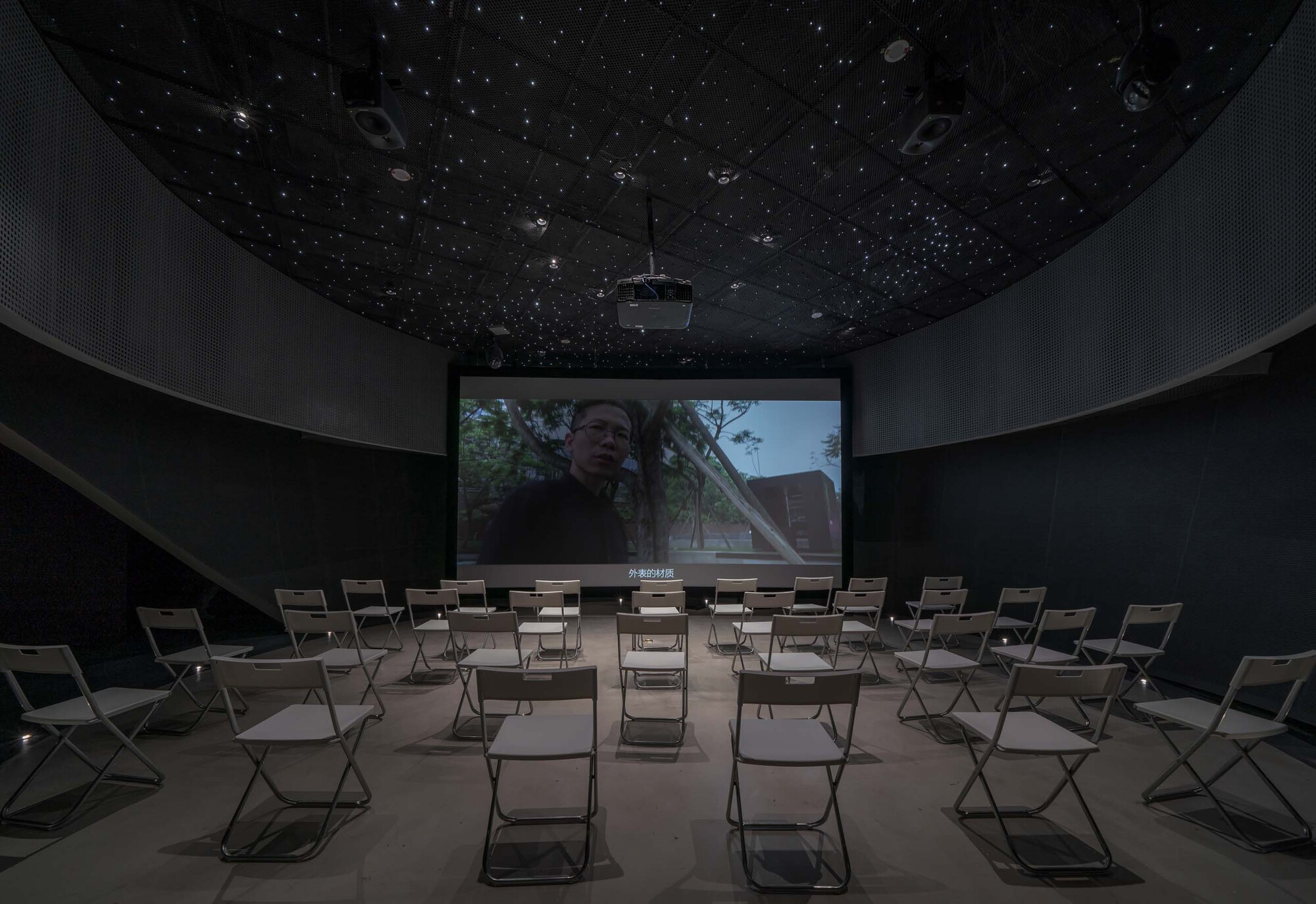 Screening room with folding chairs facing a projection under a perforated starfield ceiling