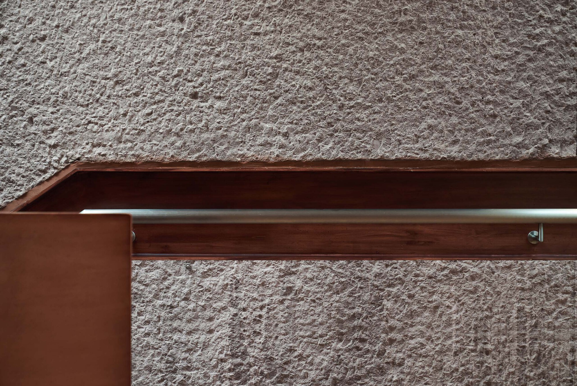 Timber handrail detail with steel rod support against a textured plaster wall