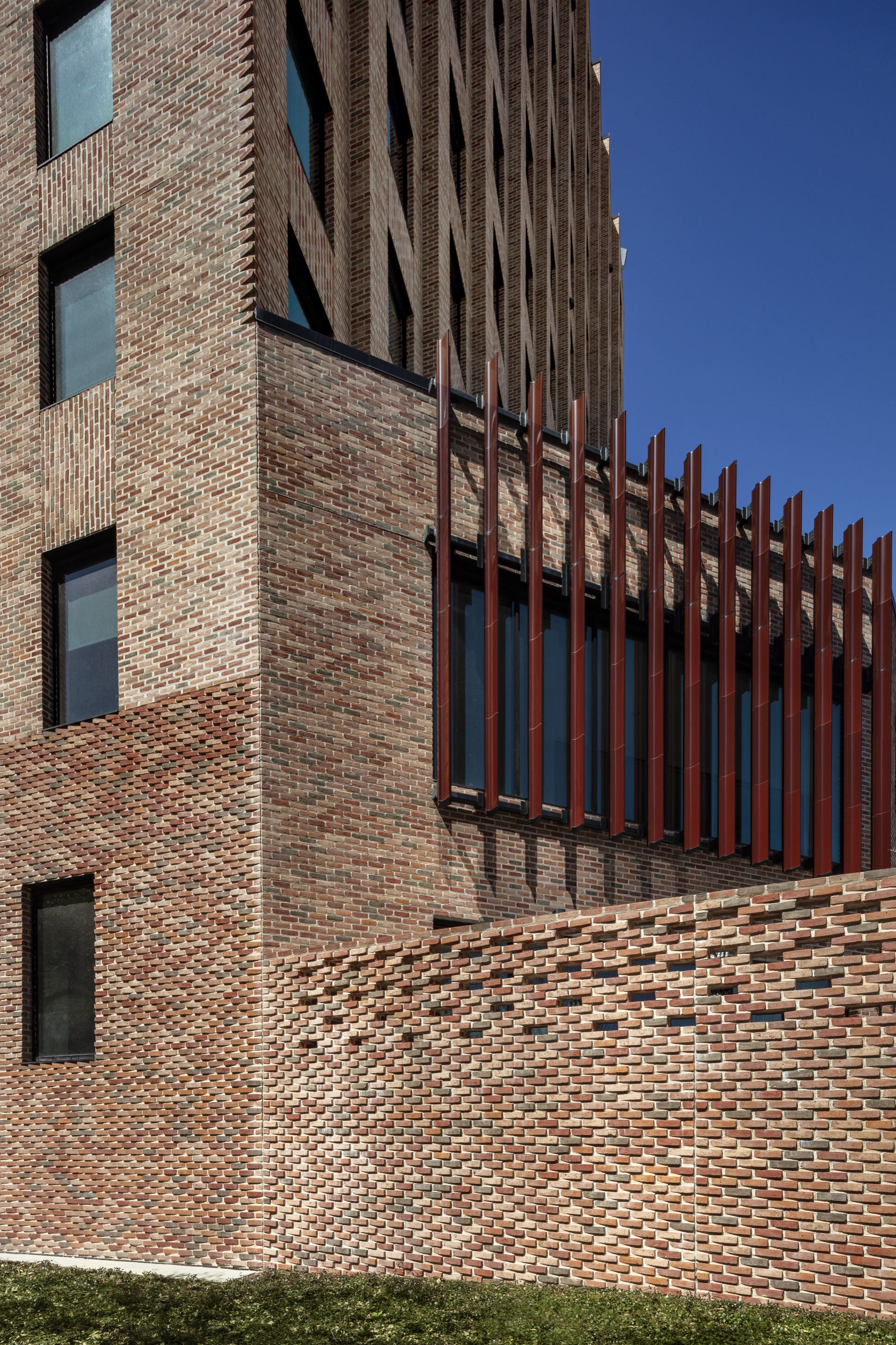 Close-up of the patterned brickwork wall meeting bronze vertical fins against a deep blue sky