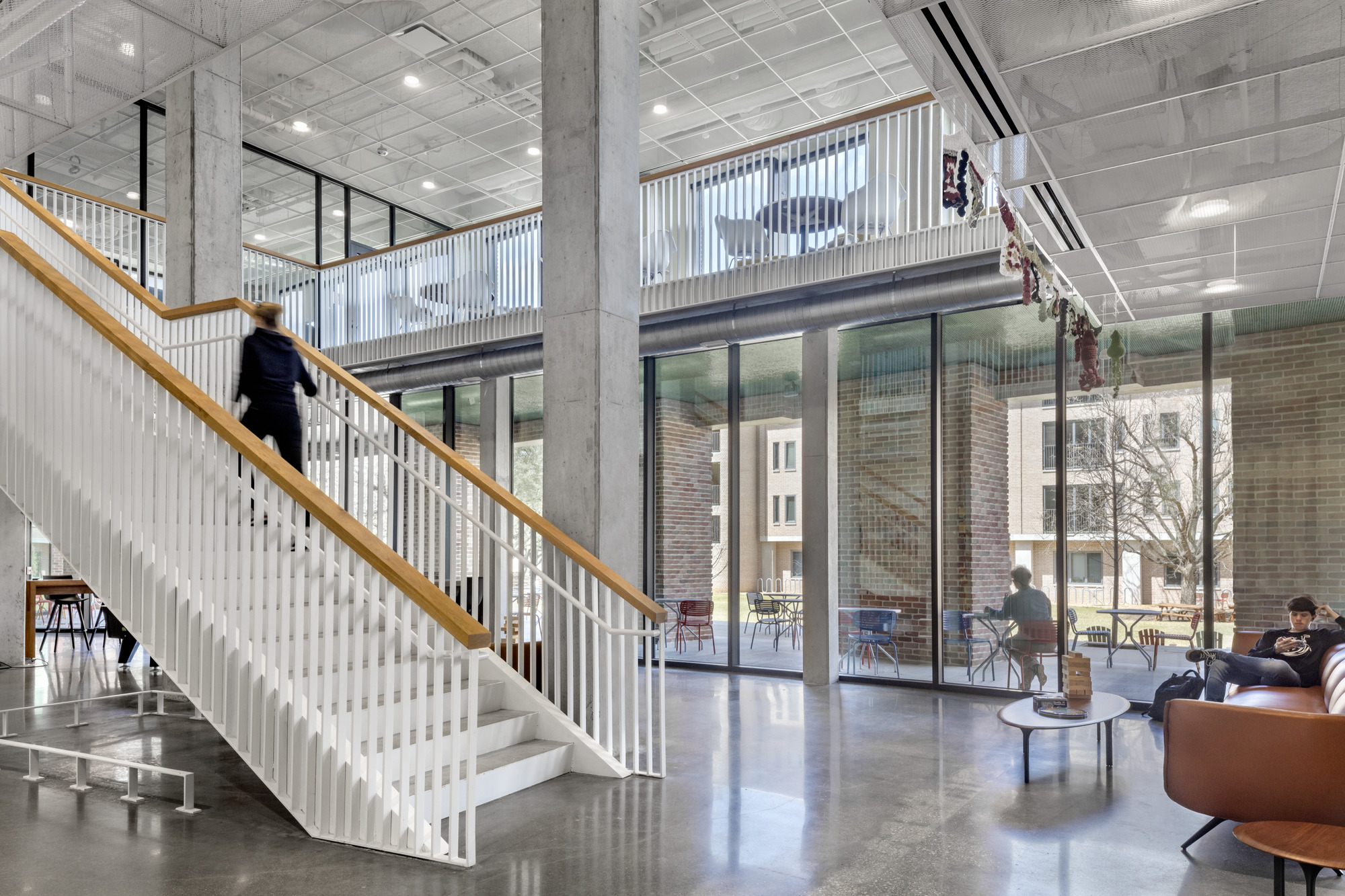 Interior view of the staircase with white vertical slats and a person ascending under exposed concrete beams
