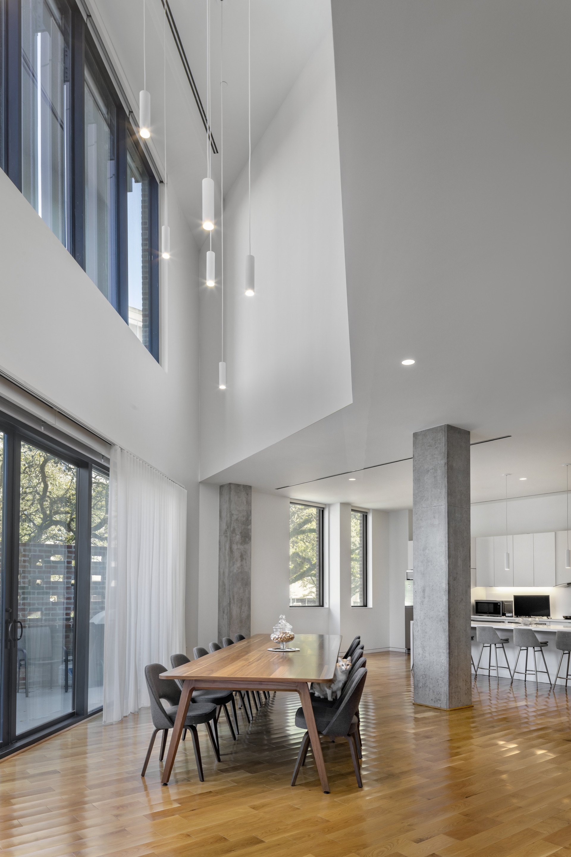 Double-height dining area with concrete columns, wood flooring, and pendant lights descending from the upper level