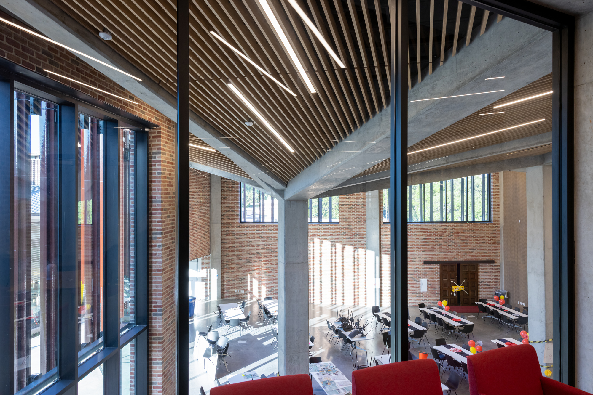 View into multi-level dining space through floor-to-ceiling glazing with exposed concrete beams and wood slat ceiling
