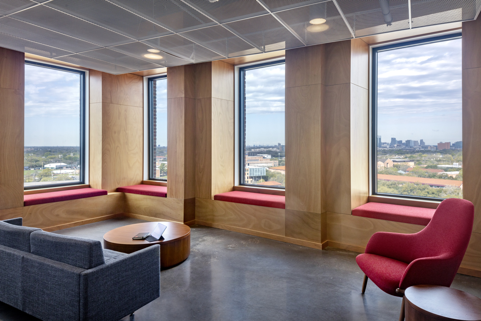 Corner lounge with three tall windows framed by timber panels and built-in crimson window seats overlooking distant skyline