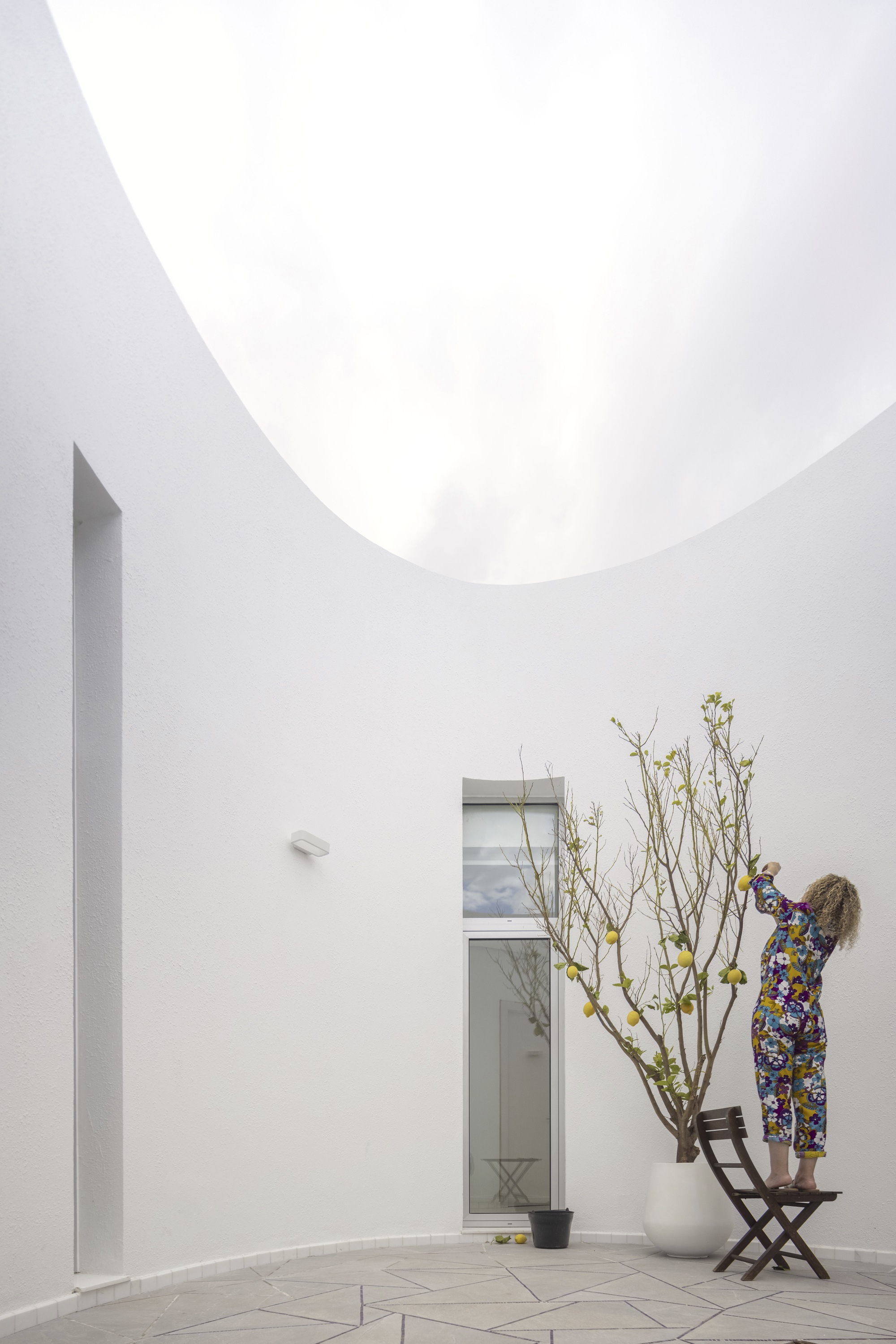 White-walled courtyard with a circular oculus overhead and a person tending to a potted tree
